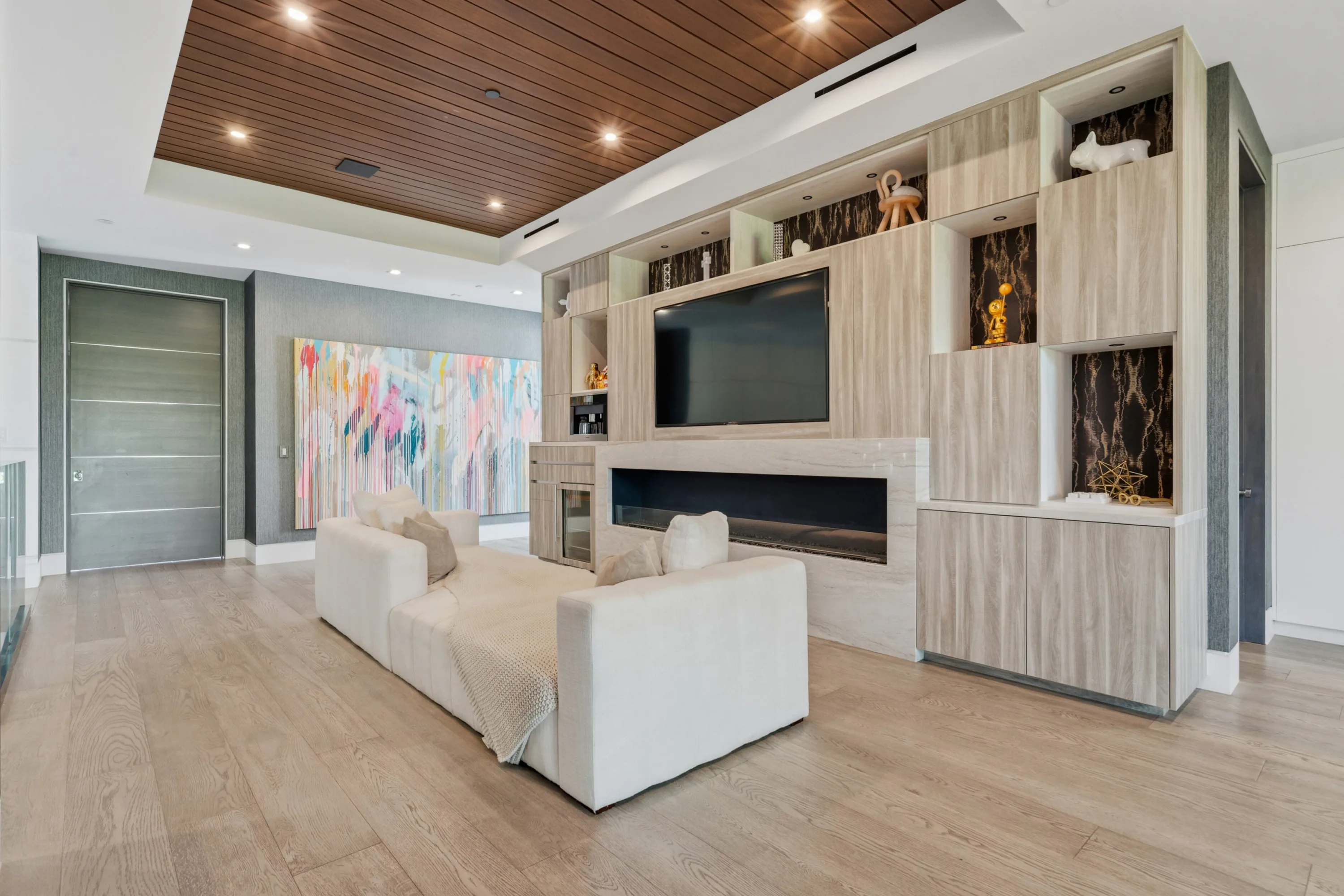 Sitting area of a bedroom suite, fireplace and screen set into pale stone joinery beside a pastel abstract canvas