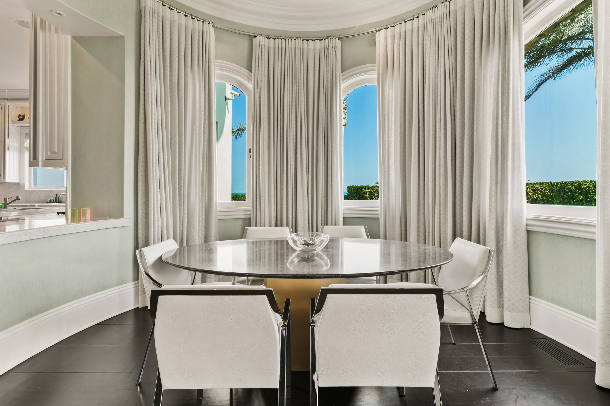 Breakfast nook in a curtained bay, round marble table for six with arched ocean windows