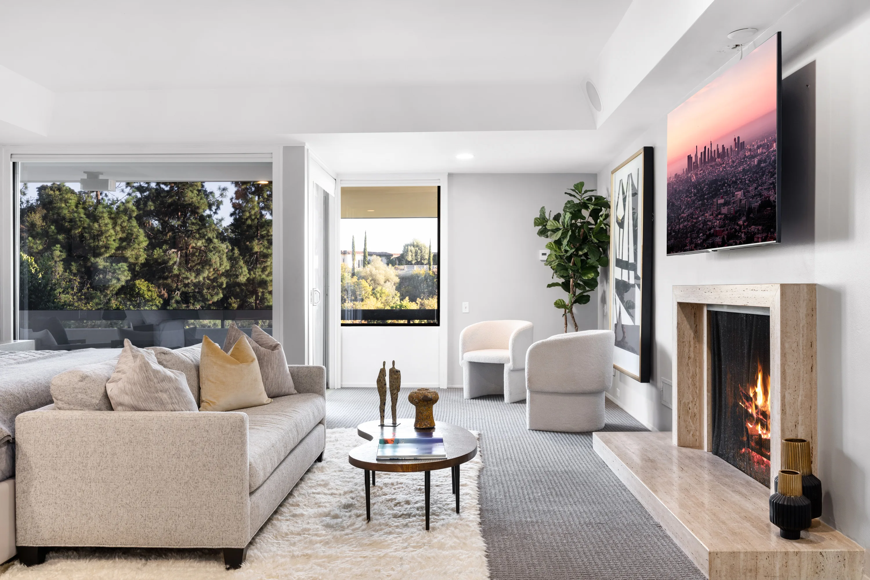 Primary suite sitting area with travertine fireplace, screen above and windows to the treeline