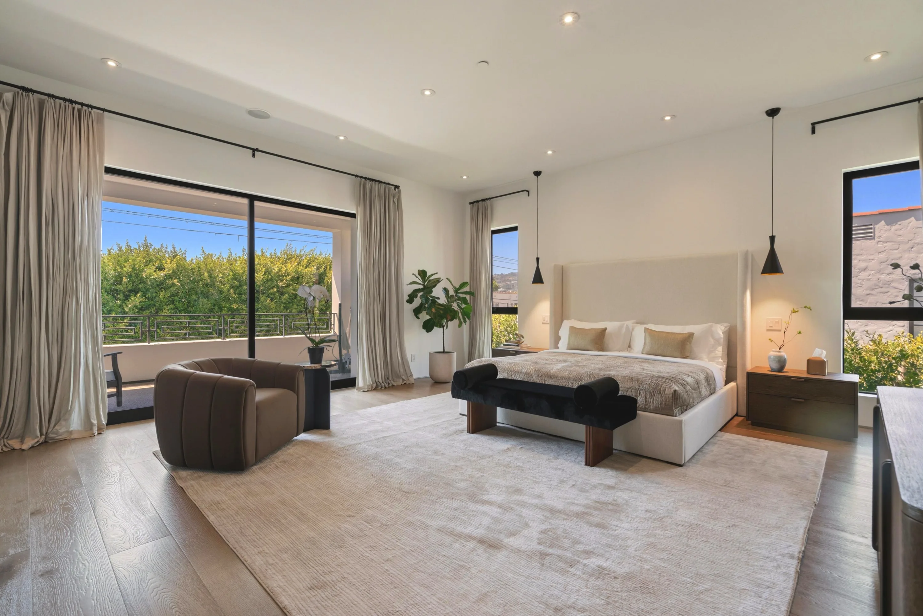 Airy bedroom with king bed, velvet bench and sliding doors to a private balcony over treetops