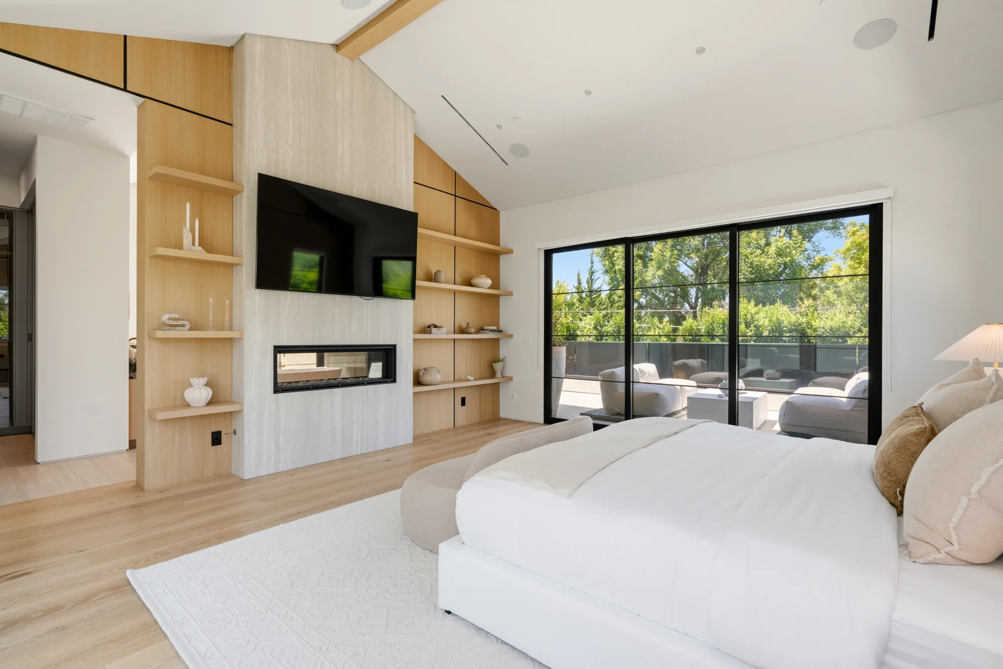 Primary bedroom fireplace and TV wall with open shelving, terrace lounge seating beyond the glass