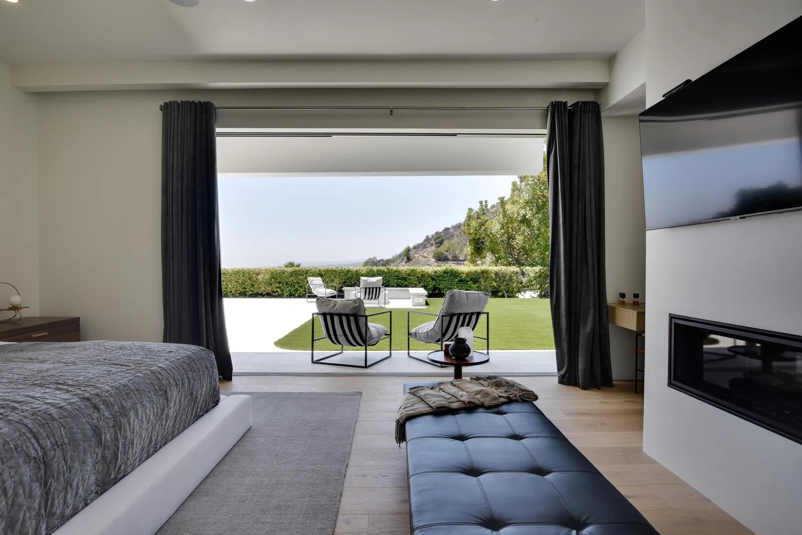 Bed facing a full-width opening onto striped patio chairs, lawn and the distant ridgeline