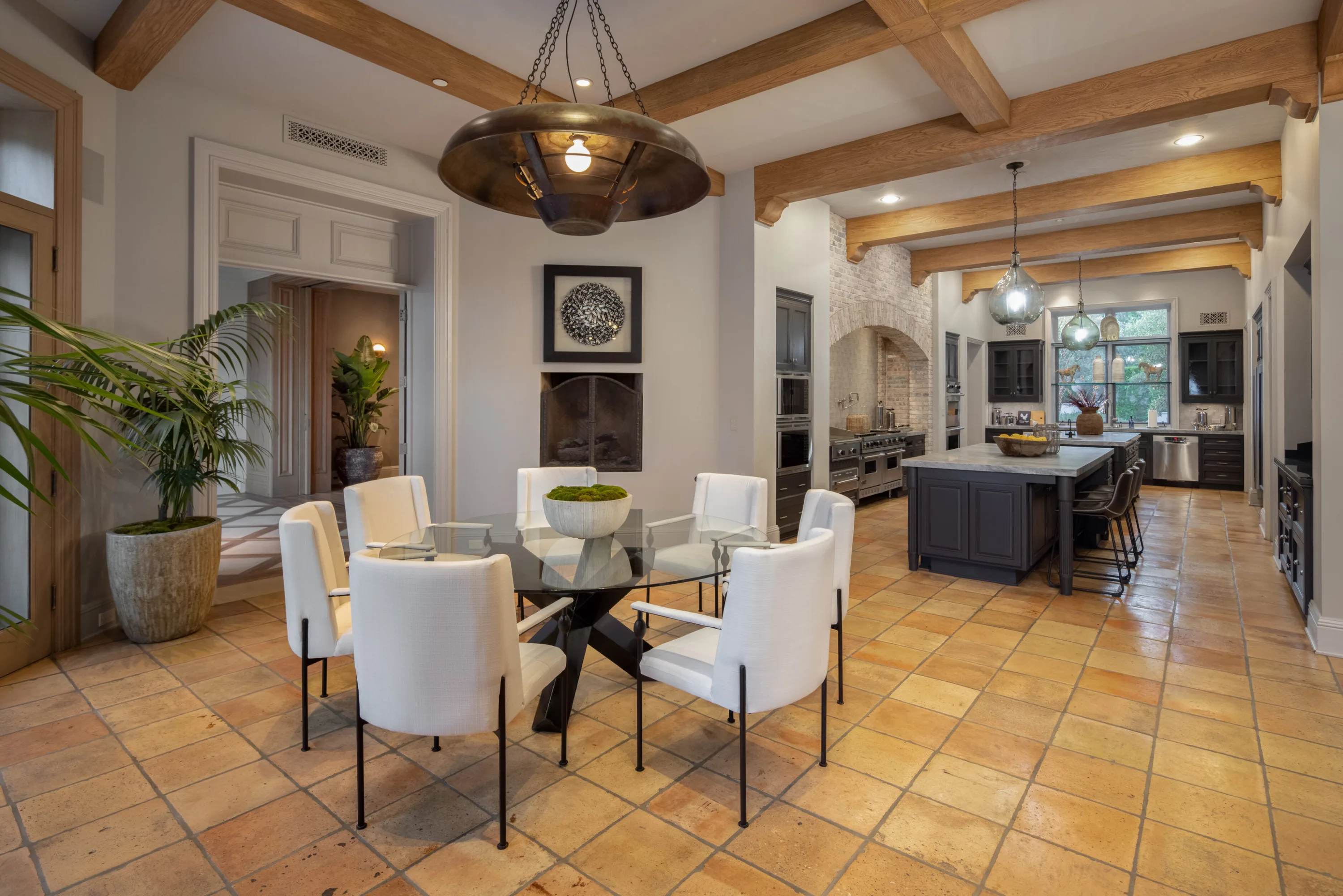 Breakfast room with round glass table beneath beamed ceilings, open to the kitchen and its island
