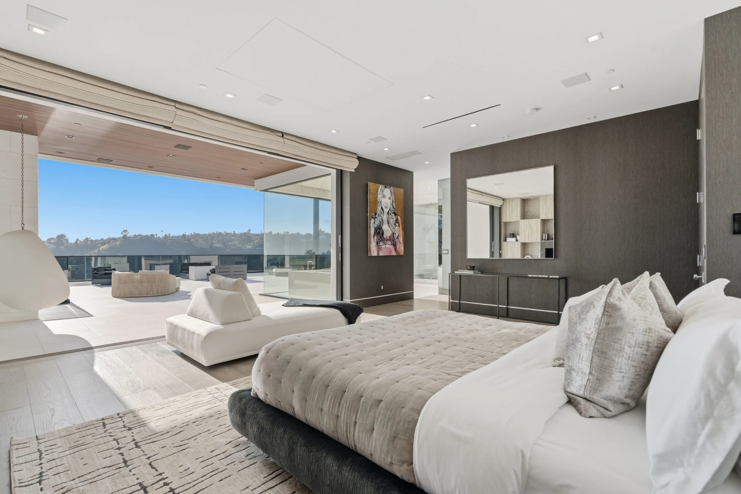Primary suite opening full-width to a private terrace, tufted king bed and hillside view in clear daylight