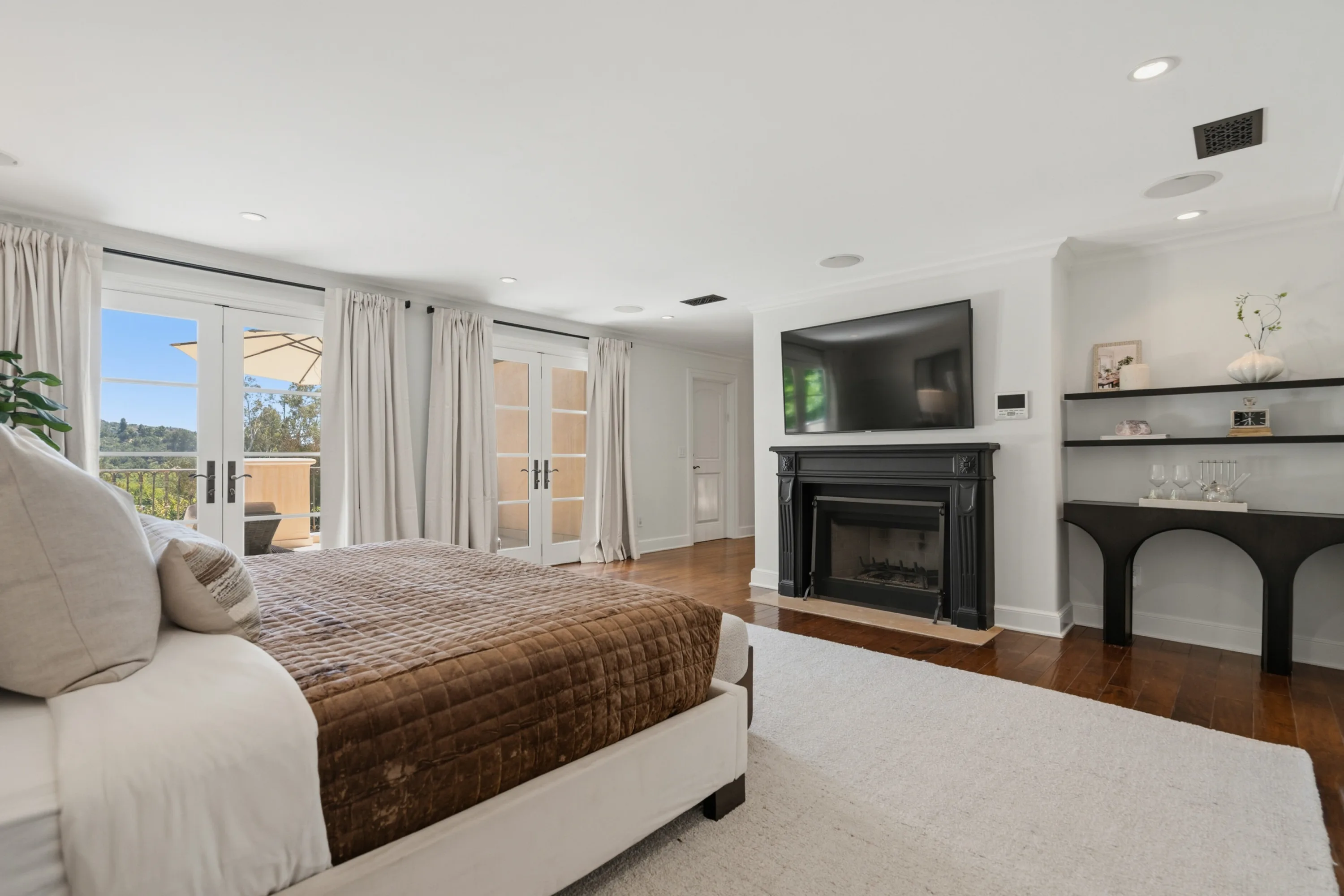 Opposite view of the primary bedroom, showing a black marble fireplace, wall-mounted TV and treetop outlook