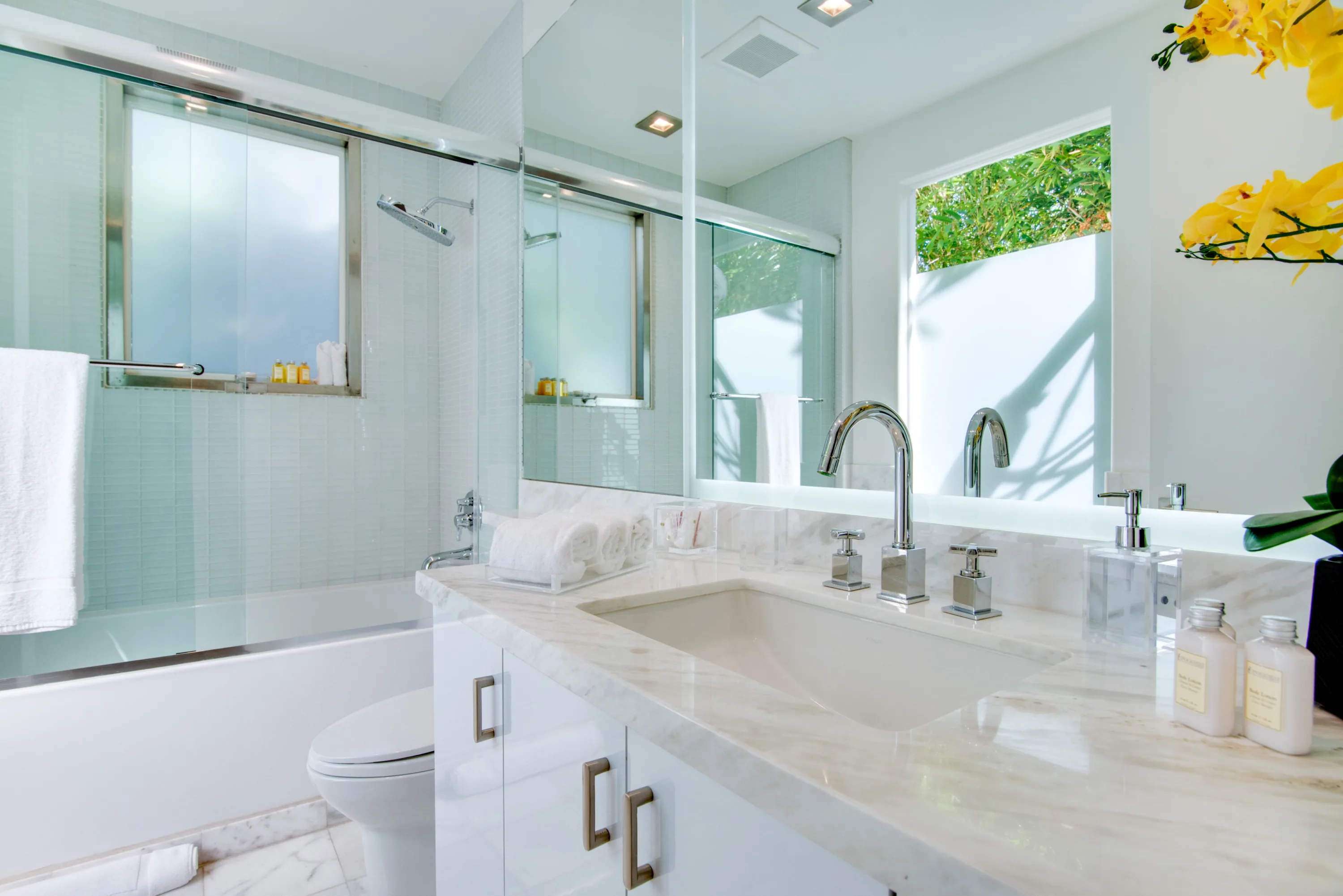 Bright bath with marble counter, soaking tub and shower, orchid stems beside the mirror