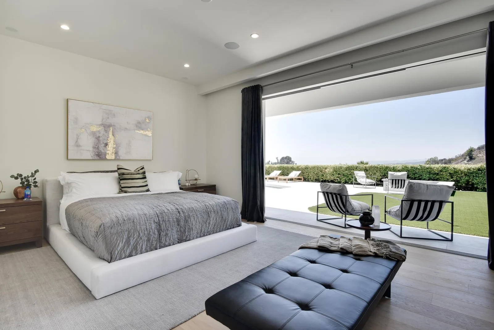 Second primary bedroom with platform bed, leather bench and glass wall open to the pool lawn