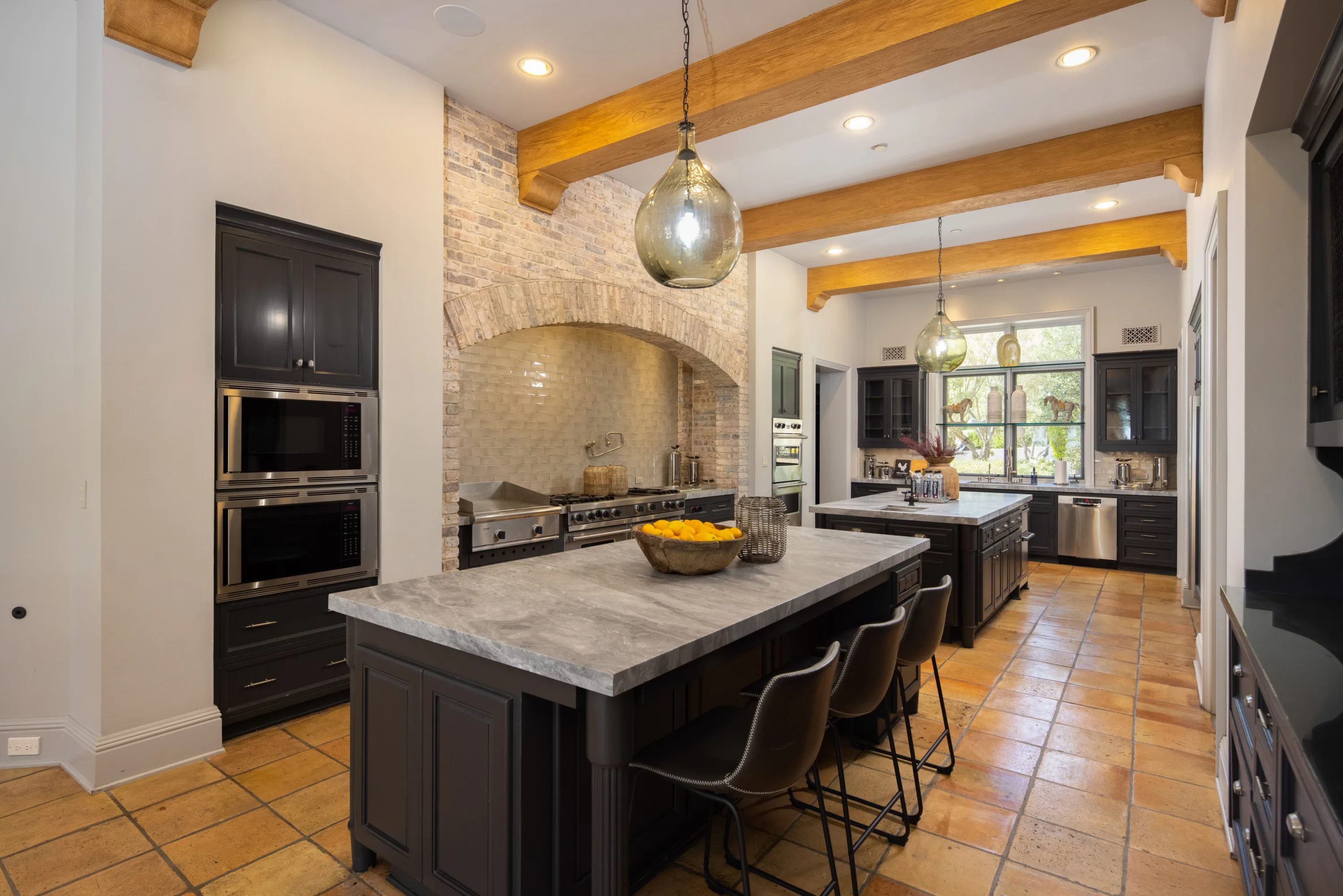 Chef's kitchen with twin islands, brick range alcove, range with griddle and terracotta tile floor