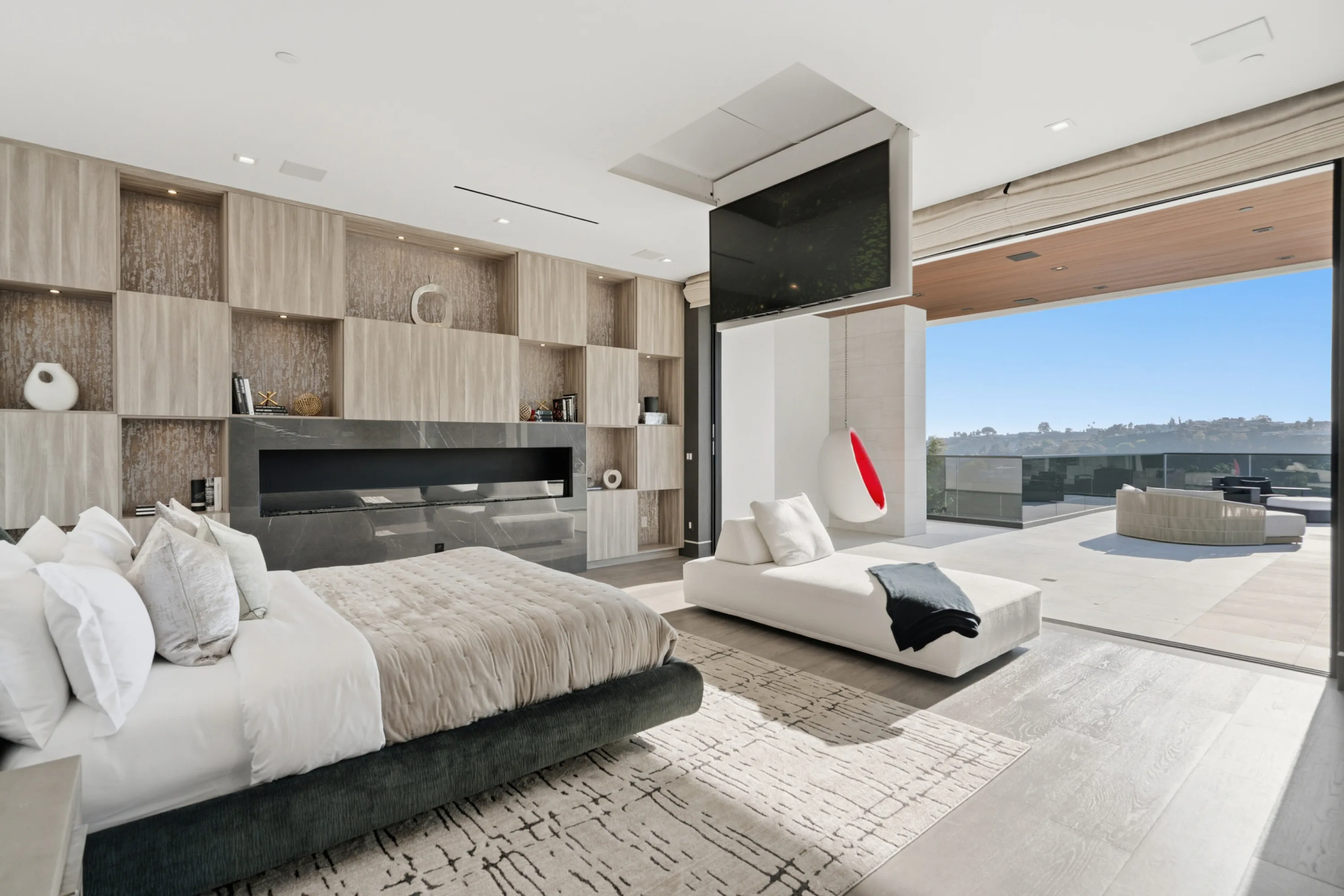Bedroom suite with stone fireplace wall, chaise and hanging egg chair on the terrace beyond the open glass