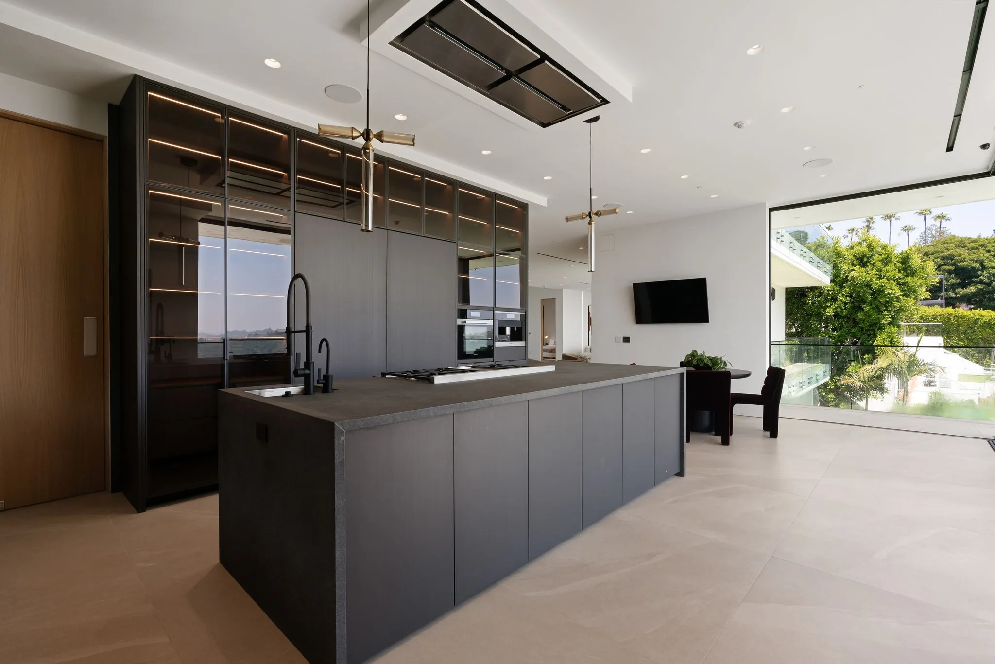 Second kitchen island with cooktop and ceiling hood, opening to a palm-filled outlook