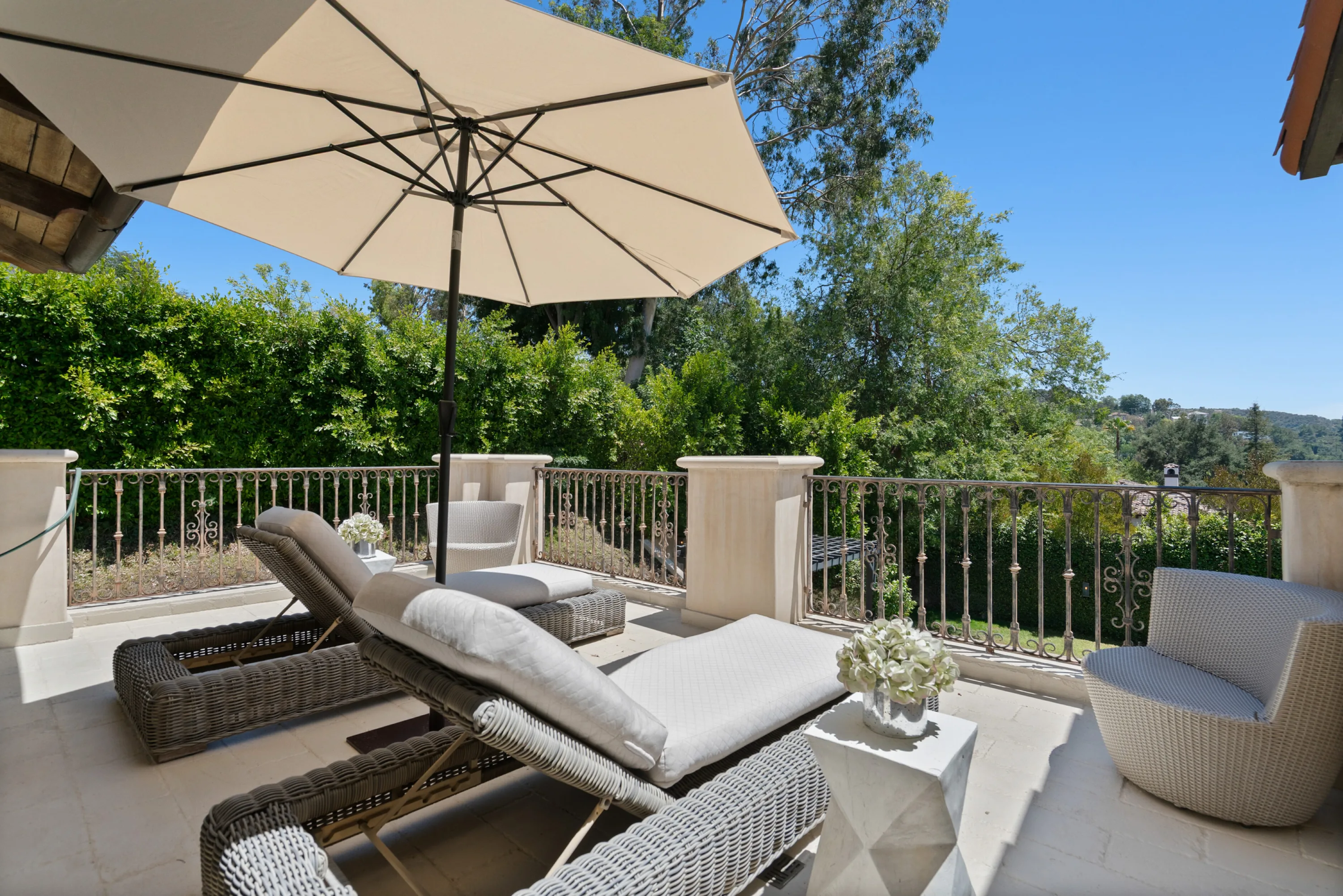 Shaded sun loungers and wicker armchairs on the primary terrace, wrought-iron railing framing the hillside greenery