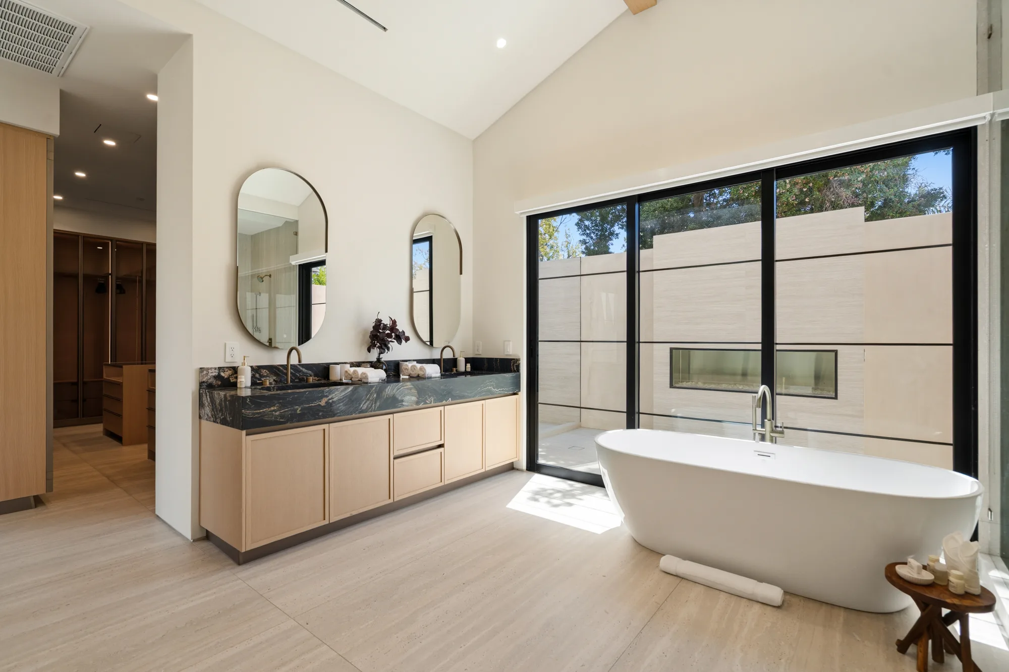 Freestanding soaking tub beside glass doors to a private outdoor shower court, walk-in closet behind