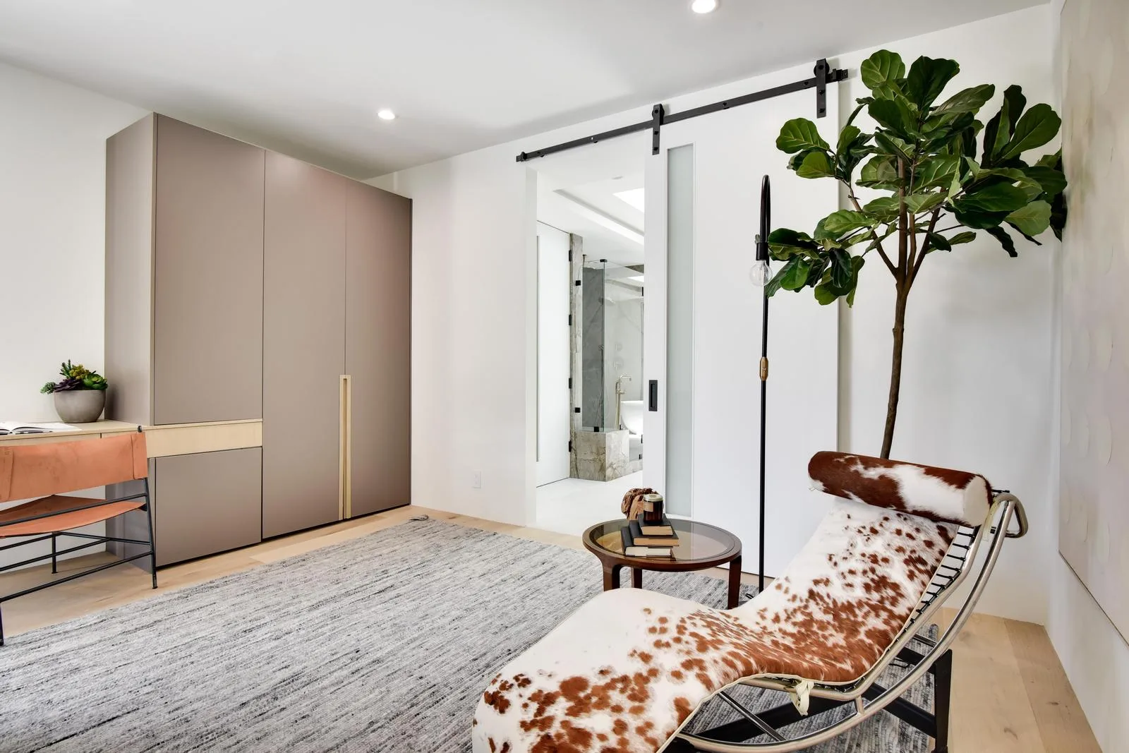 Dressing area with fitted wardrobes, a cowhide chaise and a barn door sliding through to the marble bath