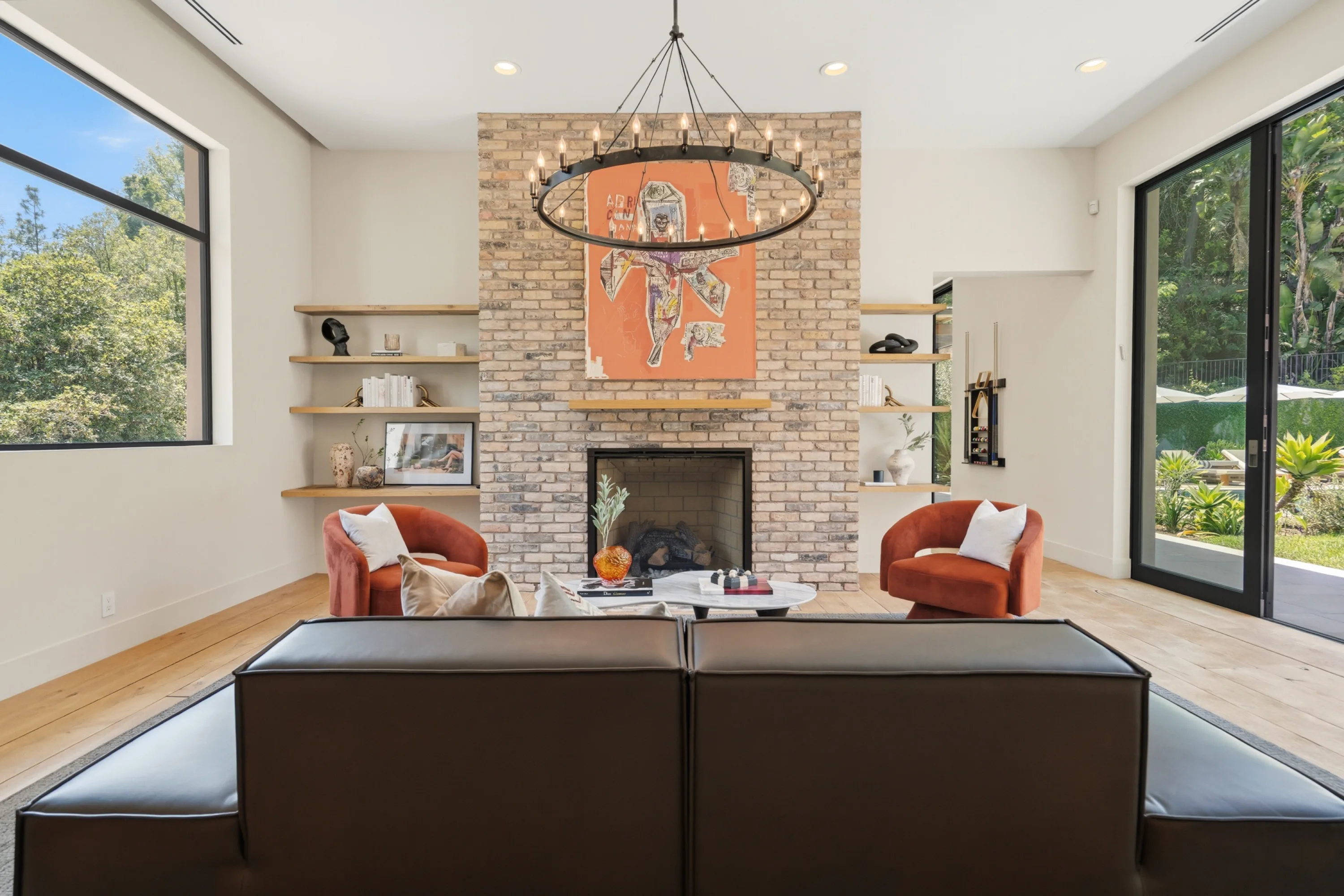 Living room anchored by a brick fireplace, iron chandelier and rust armchairs, sliding doors open to the pool