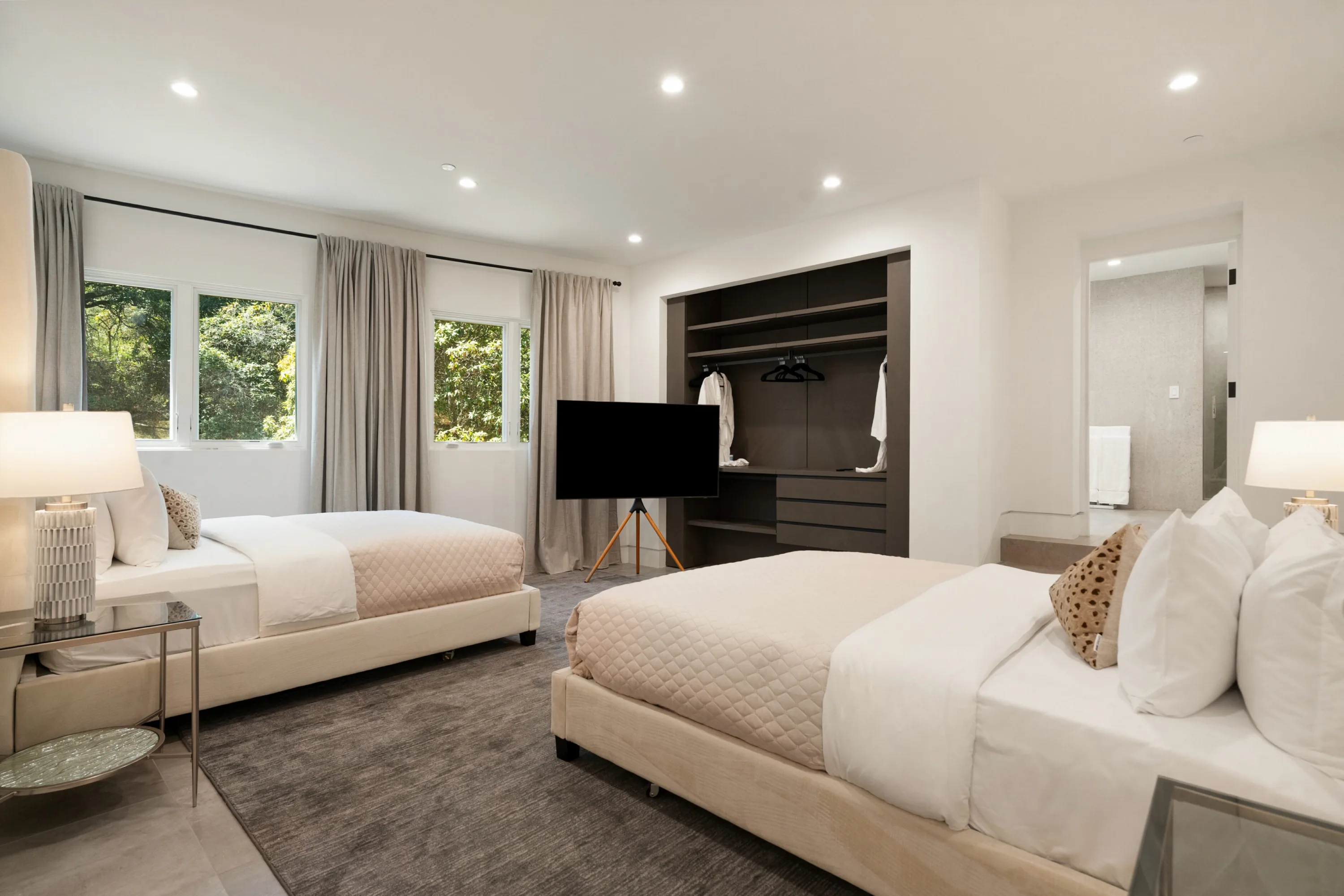 Twin-bed guest room with open dressing wardrobe, robes and a TV on a tripod stand