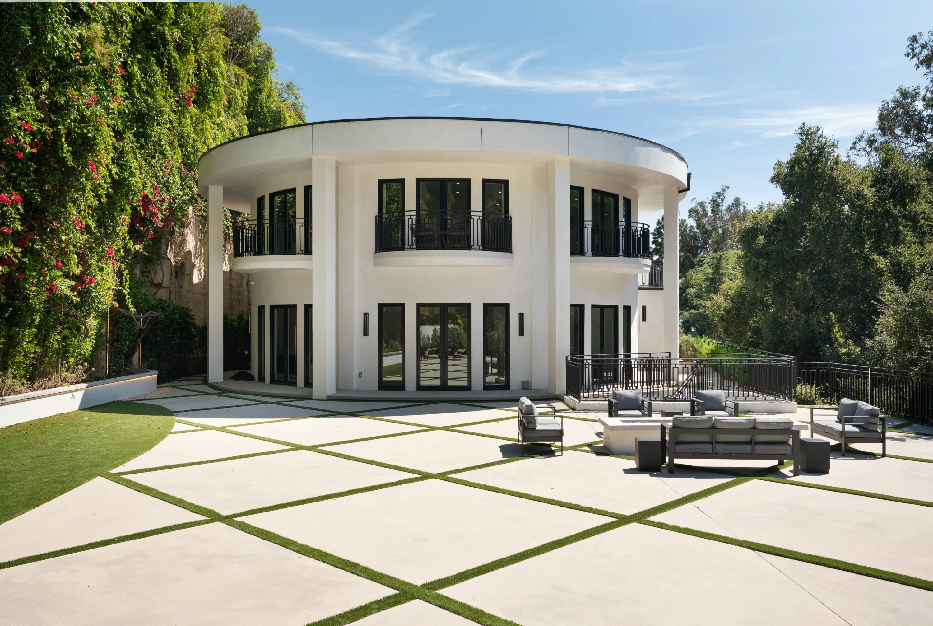 Curved white façade of the Brentwood estate above a grass-veined terrace and fire-pit seating