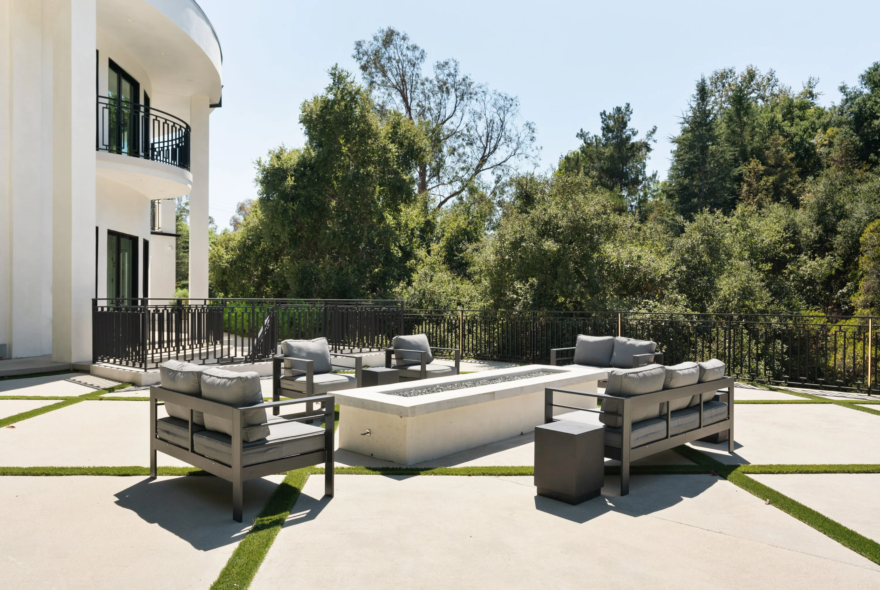 Sunken fire table ringed by cushioned armchairs on the terrace, treetops beyond the railing