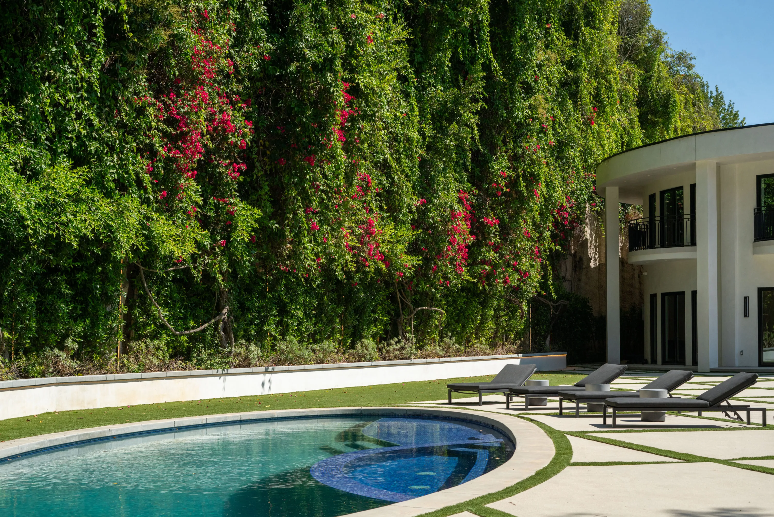 Oval pool and row of loungers beneath a towering wall of bougainvillea-covered greenery