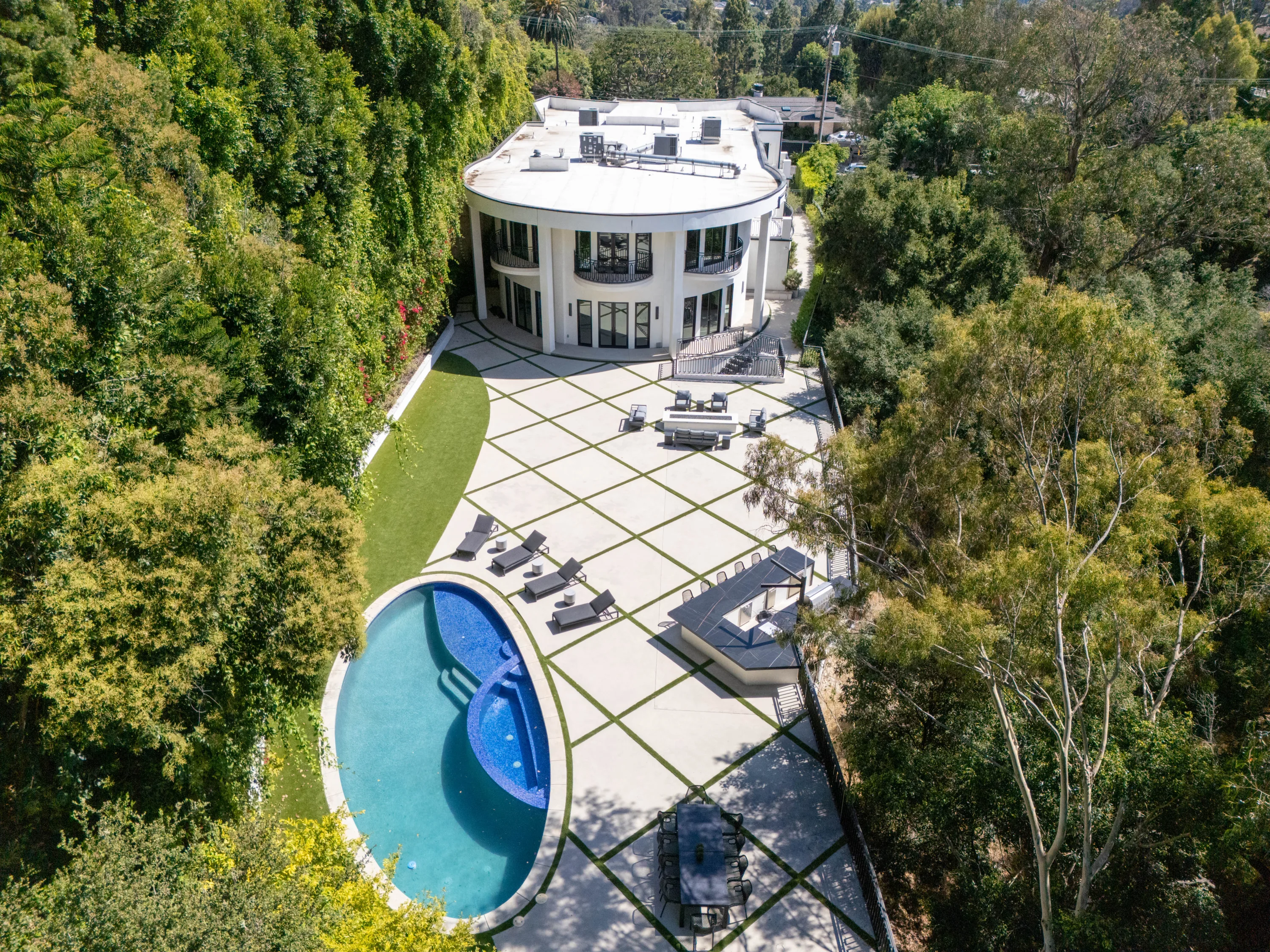 Aerial view of the rotunda-shaped house, kidney pool and vast paved terrace hemmed by trees