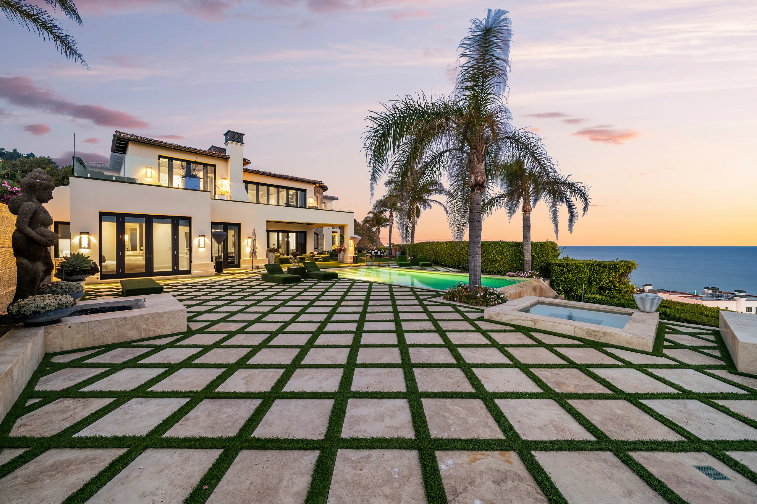 Carbon Estate at dusk: grass-seamed stone terrace, lit pool, sunken spa and the ocean beyond the palms
