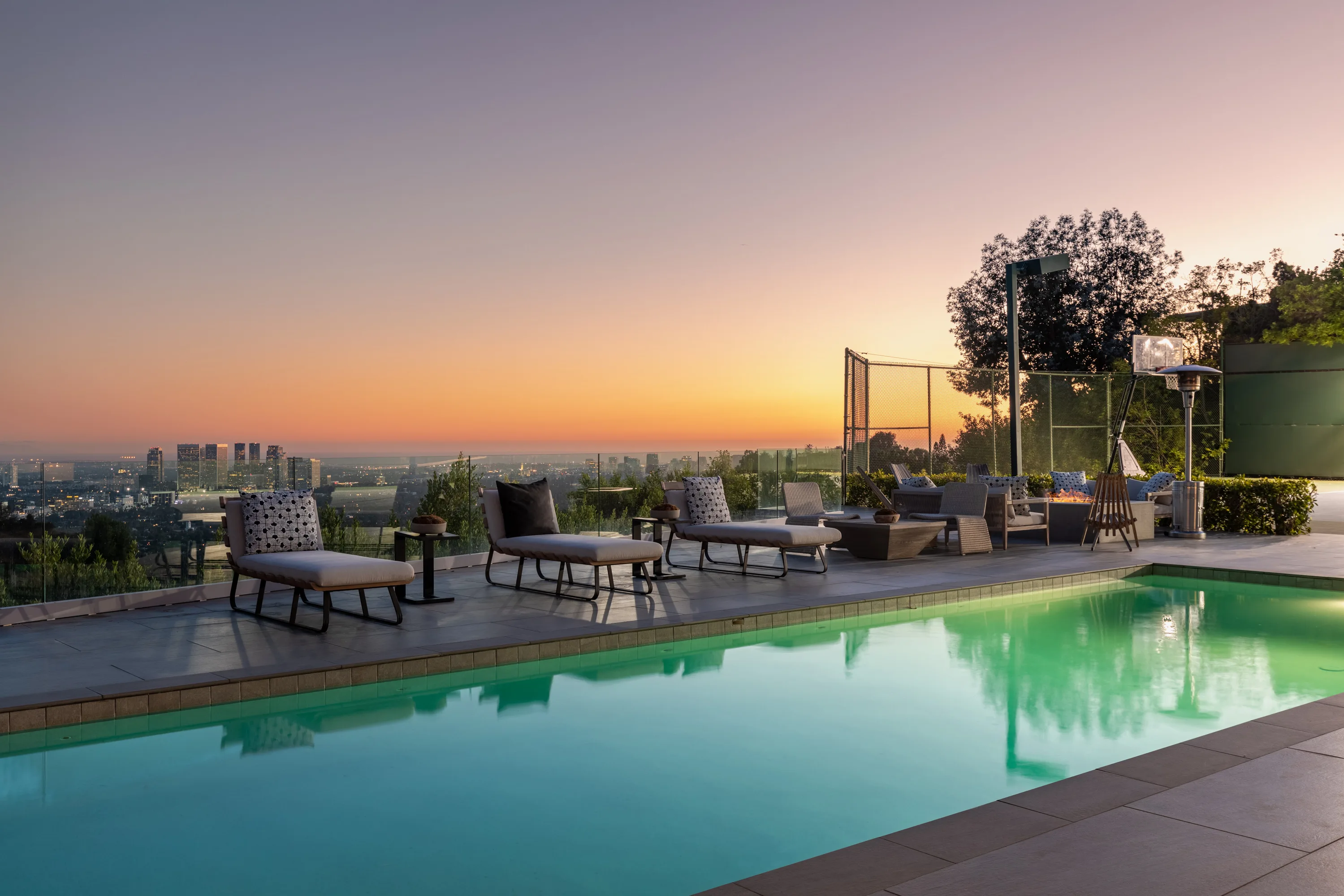 Zero-edge pool and sun loungers facing a city-to-ocean skyline at sunset