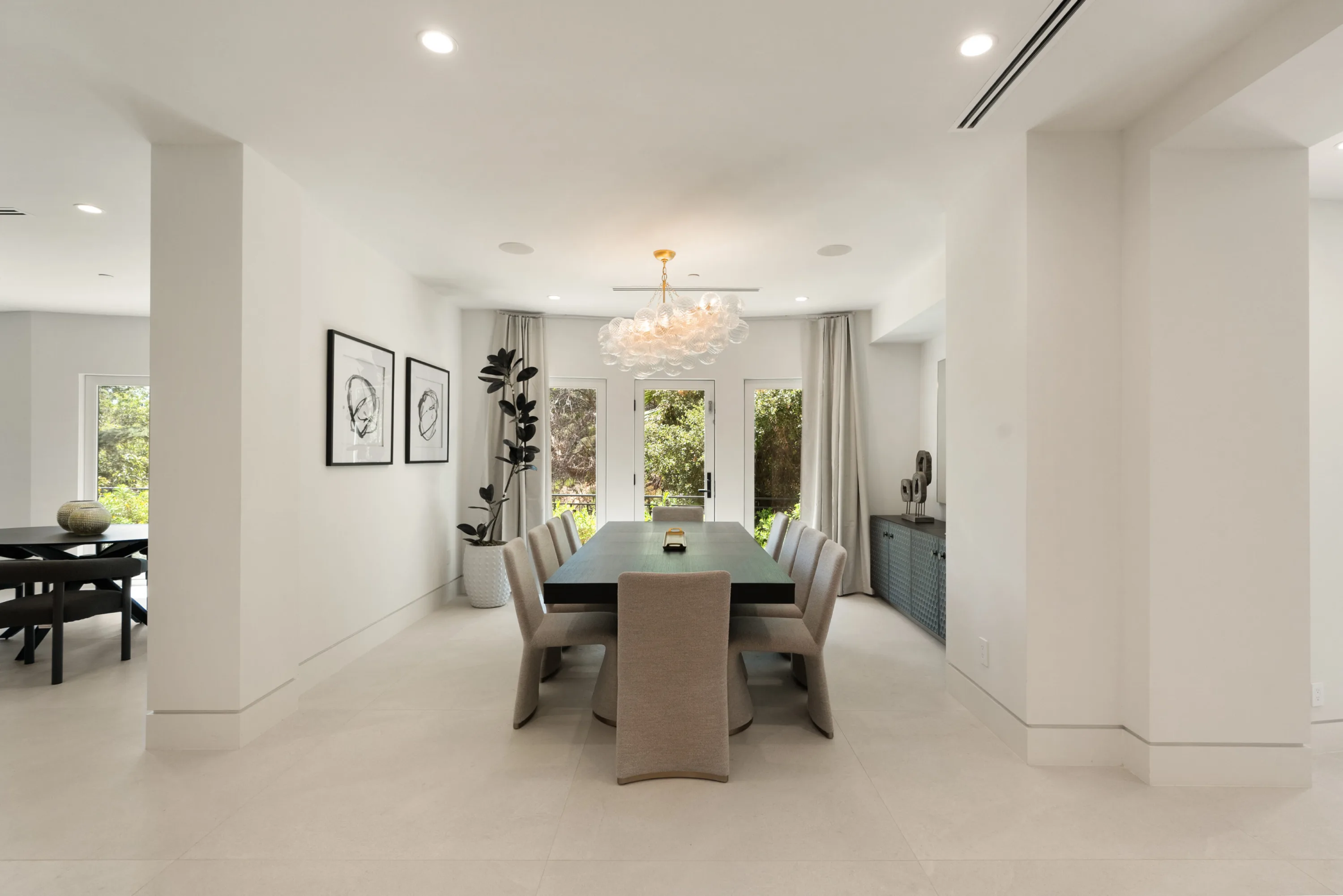 Formal dining room seating eight beneath a cluster-glass chandelier, garden doors behind