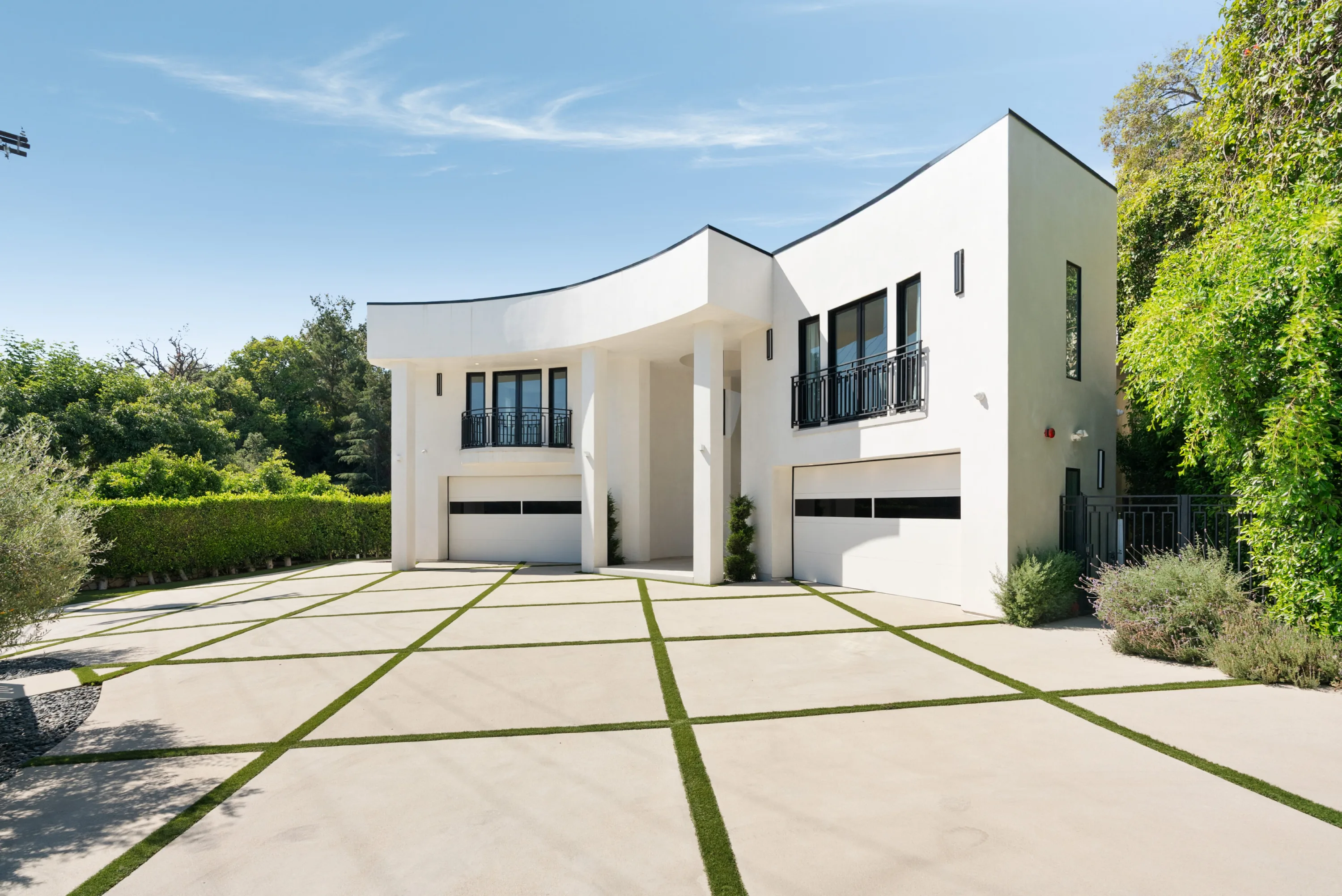 Wide angled view of the gated motor court and two-car garage wings framed by mature hedging