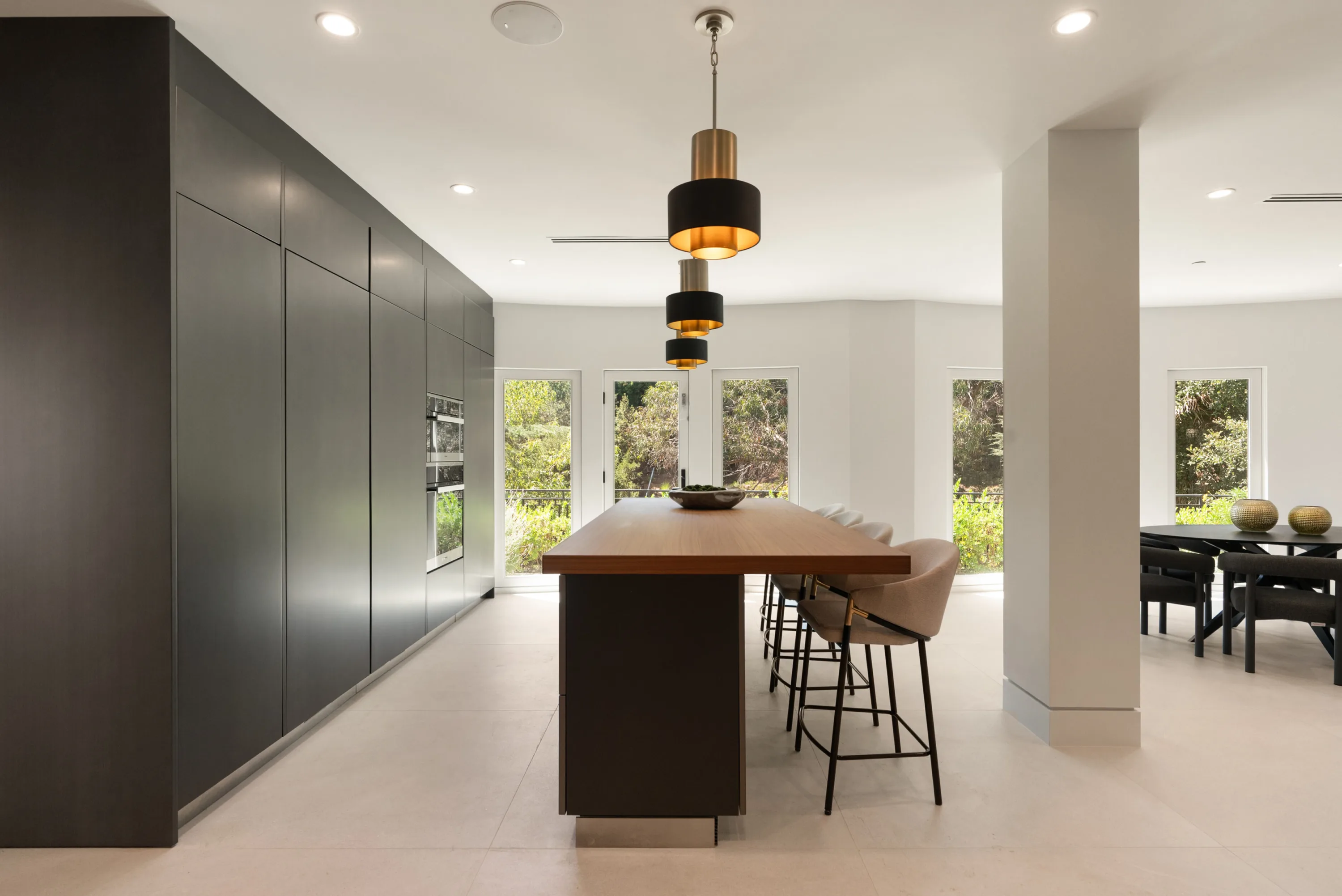 Walnut-topped island with counter stools running toward the casual dining area under brass pendants
