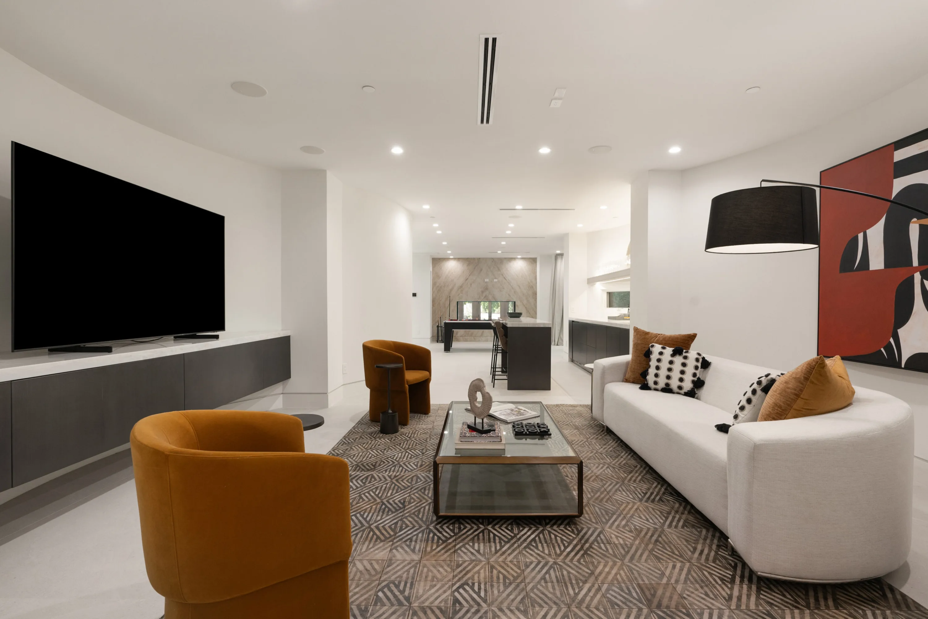 Media lounge with oversized wall-mounted screen, curved white sofa and ochre velvet armchairs