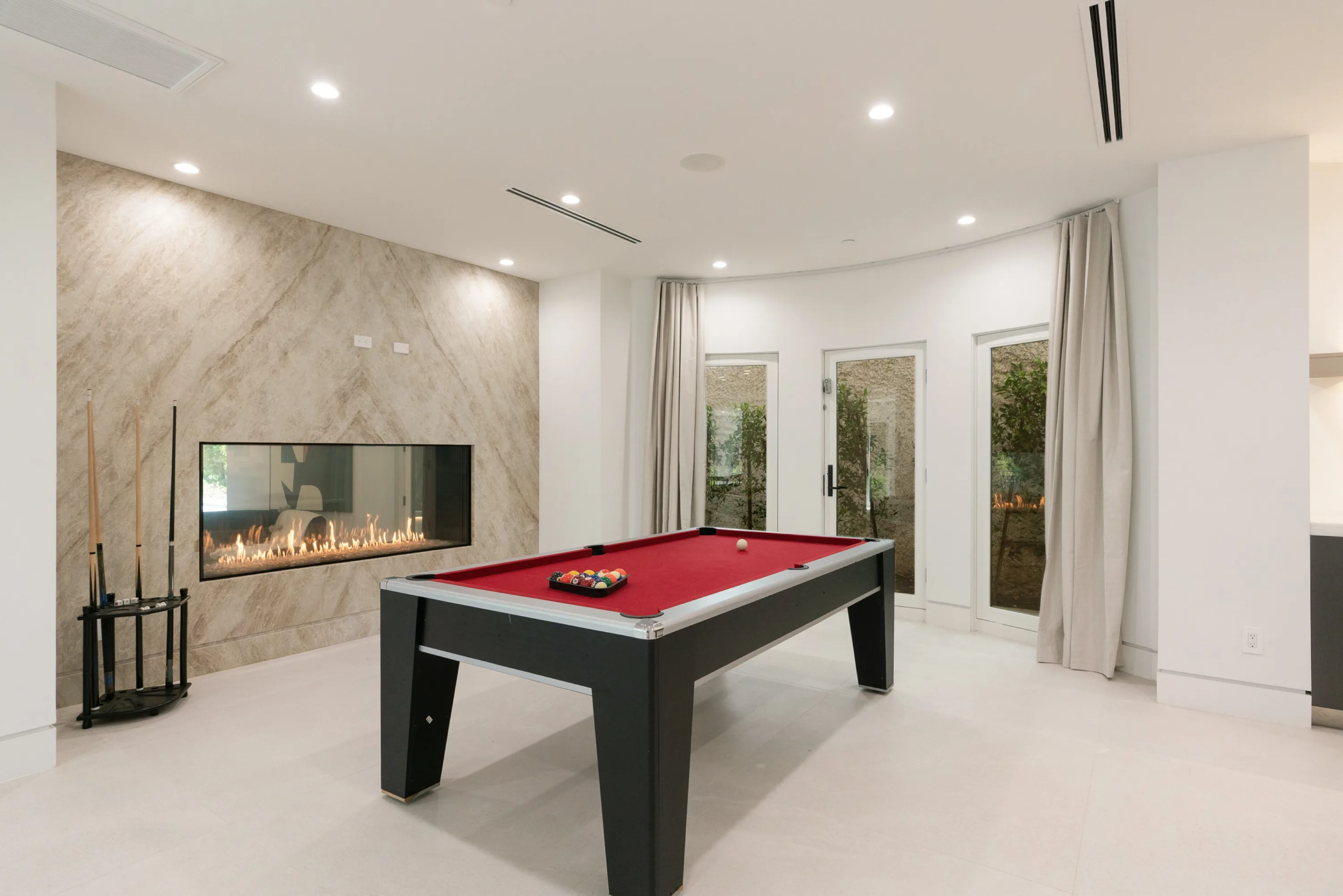 Games room with red-felt pool table set against a linear fire in a full-height stone wall