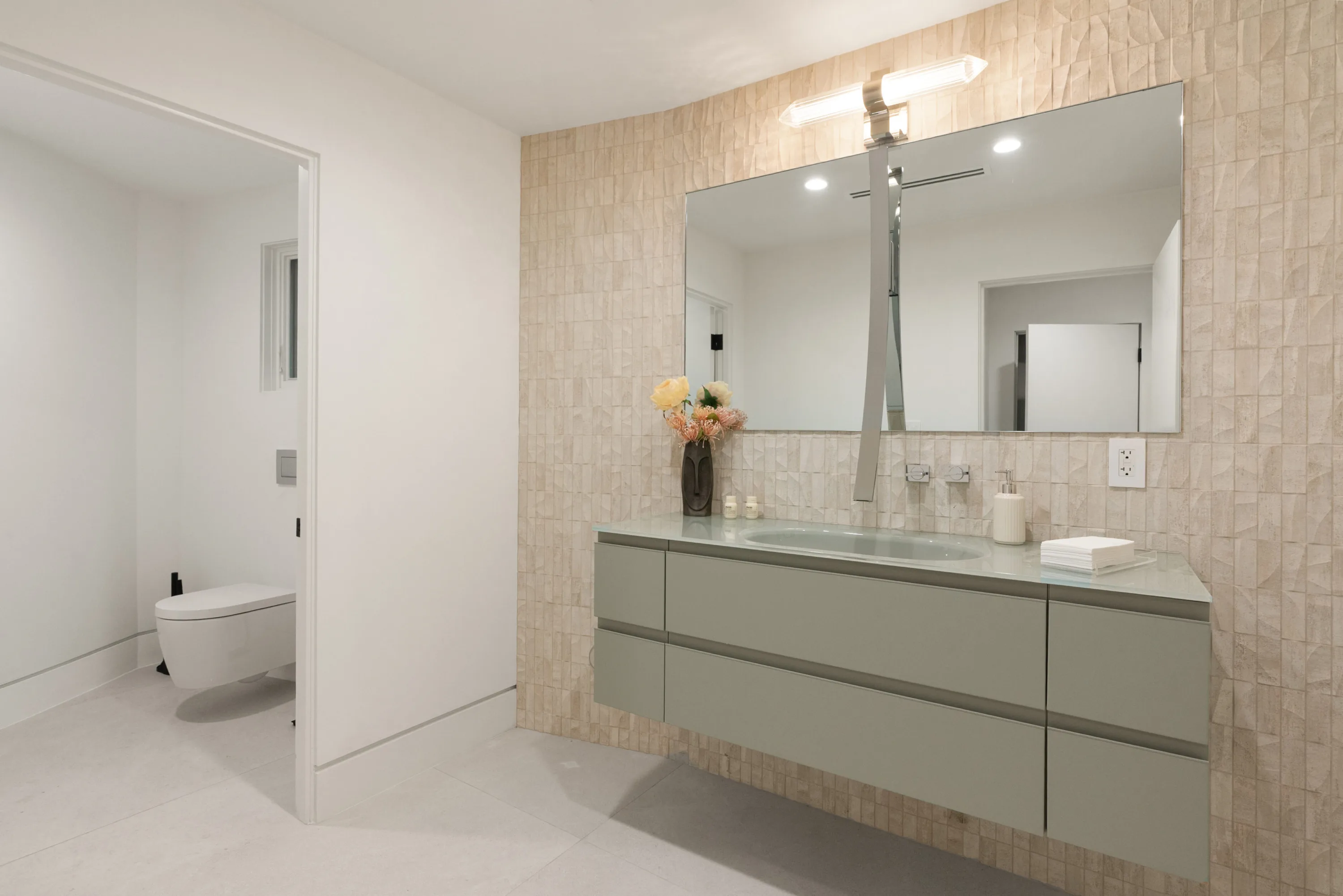 Guest bathroom with floating sage vanity, textured stone wall and separate enclosed water closet