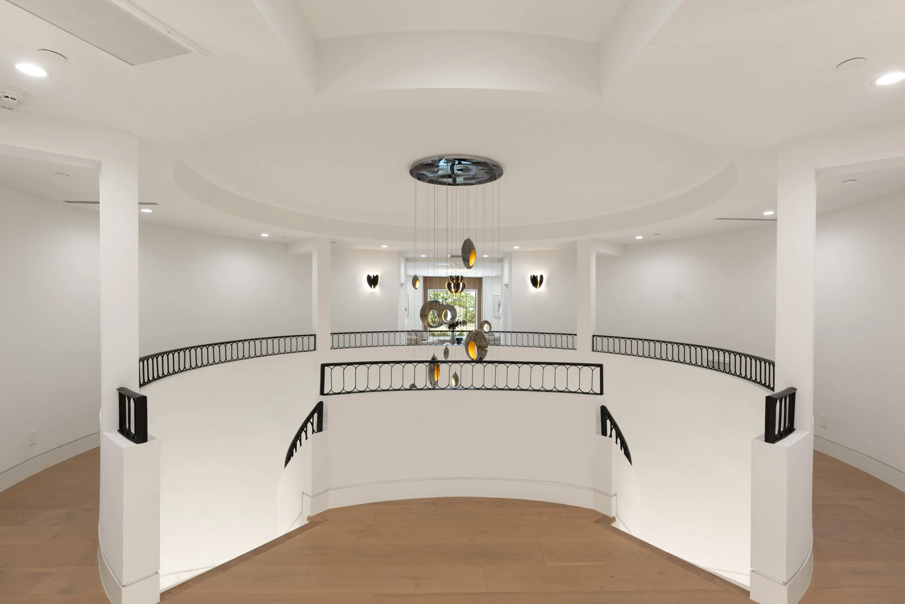Curved upper landing overlooking the stair void, cascading pendant sculpture at its centre