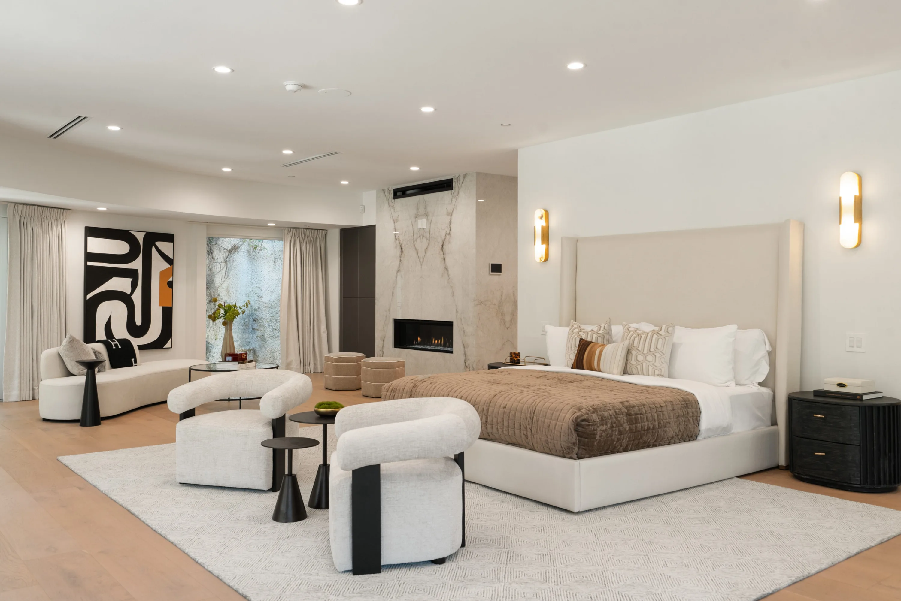 Primary bedroom from the opposite side, tall upholstered headboard facing a marble-clad linear fireplace