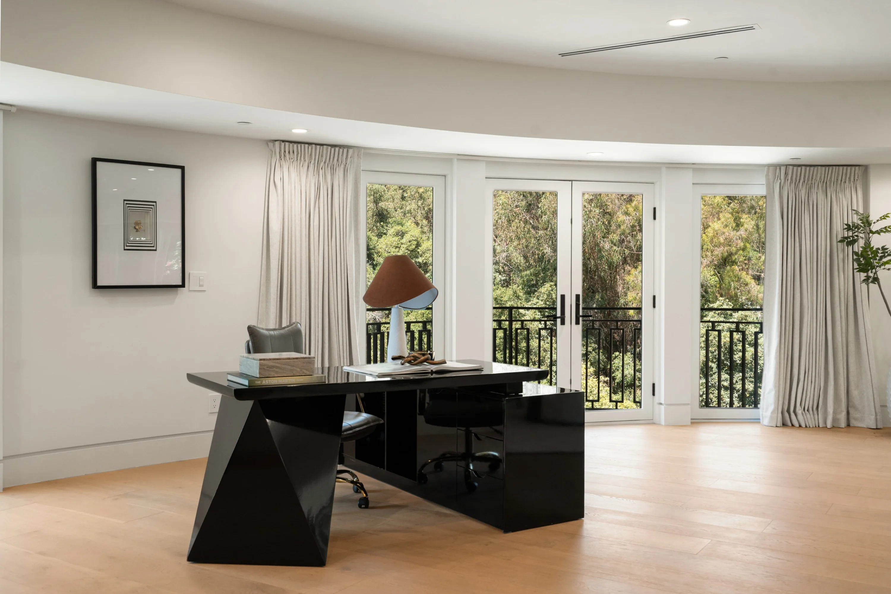 Home office with sculptural black lacquer desk set before balcony doors and canopy views