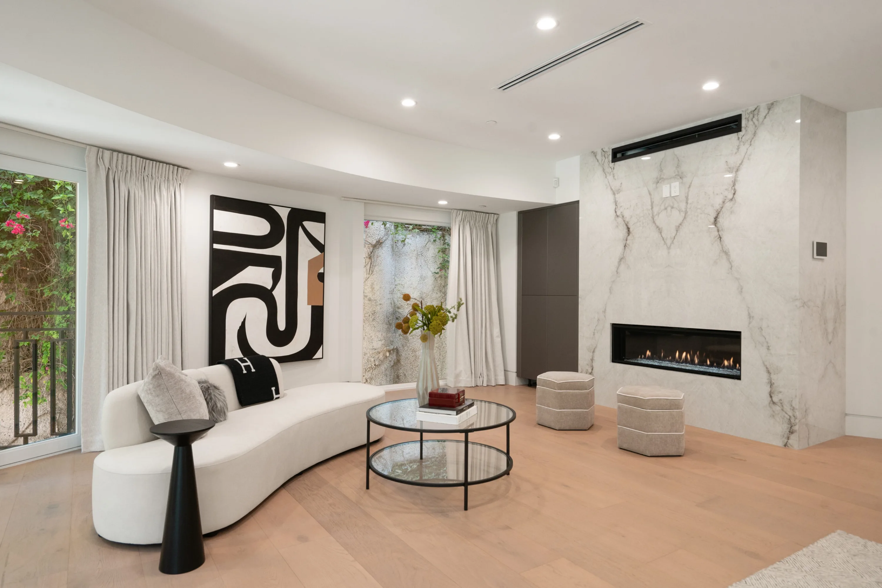 Primary suite sitting area with curved white sofa facing a linear fireplace set into a full-height marble wall