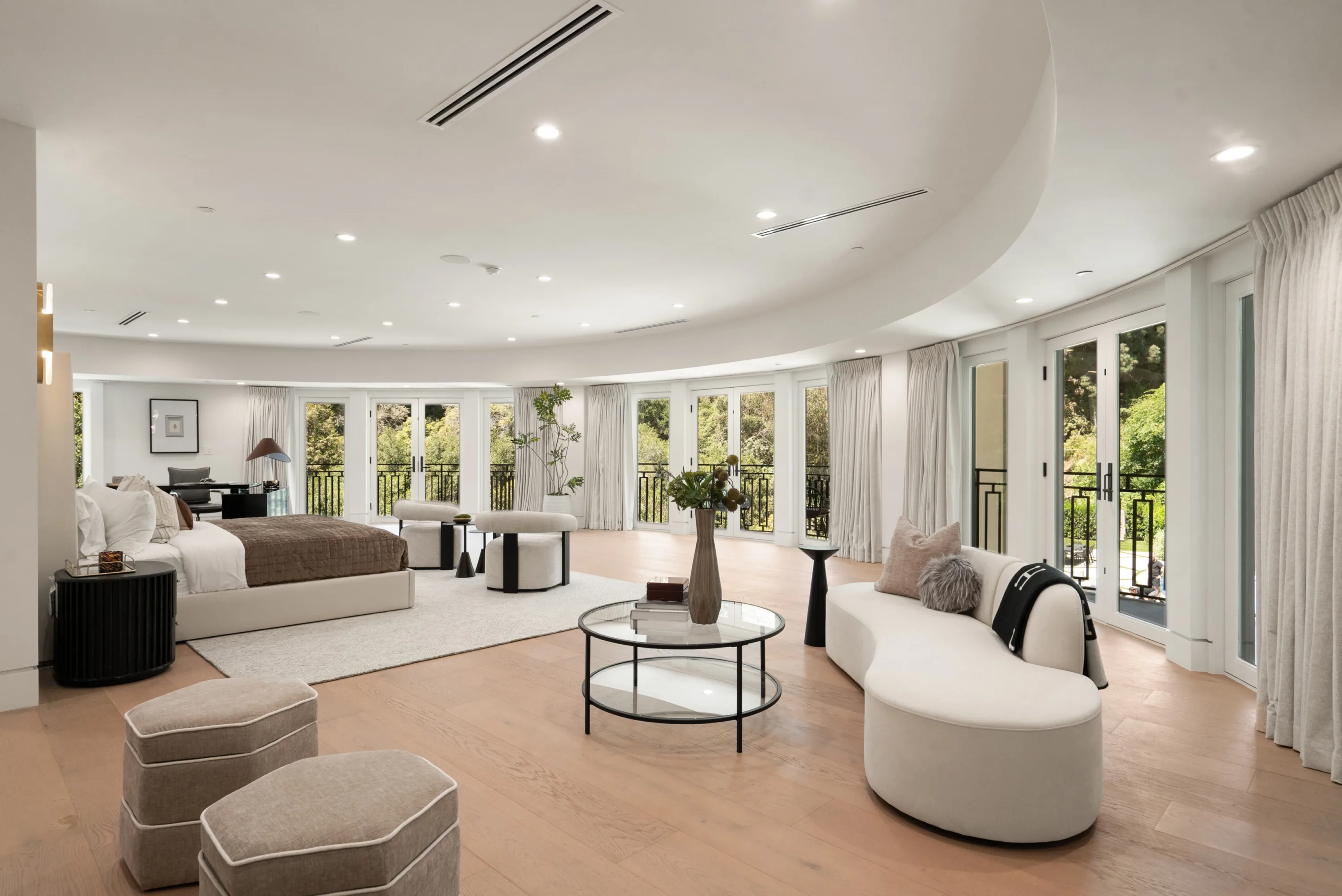 Sweeping primary suite with king bed, curved lounge sofa and a wall of French doors opening to treetop balconies