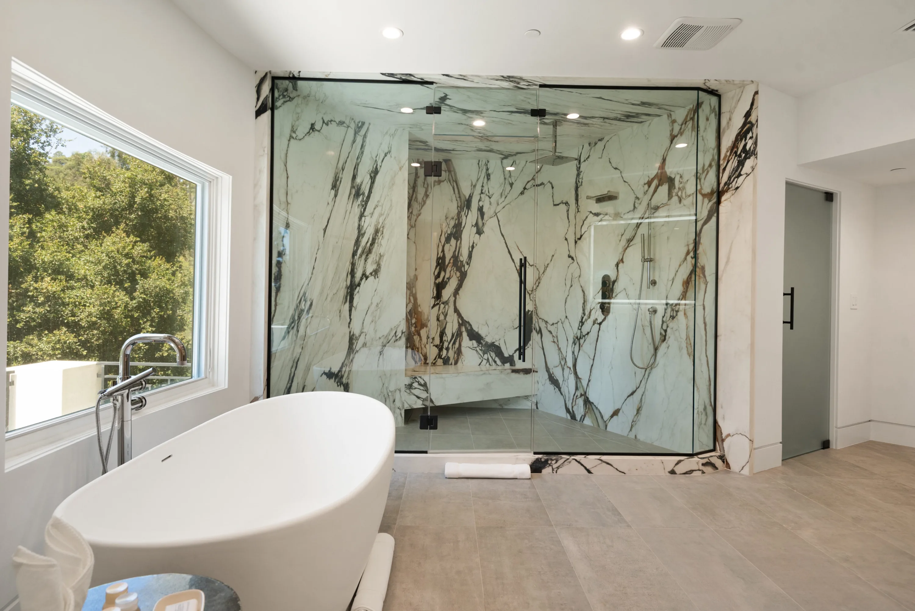 Glass-walled steam shower clad in dramatic veined marble, beside the sculptural soaking tub