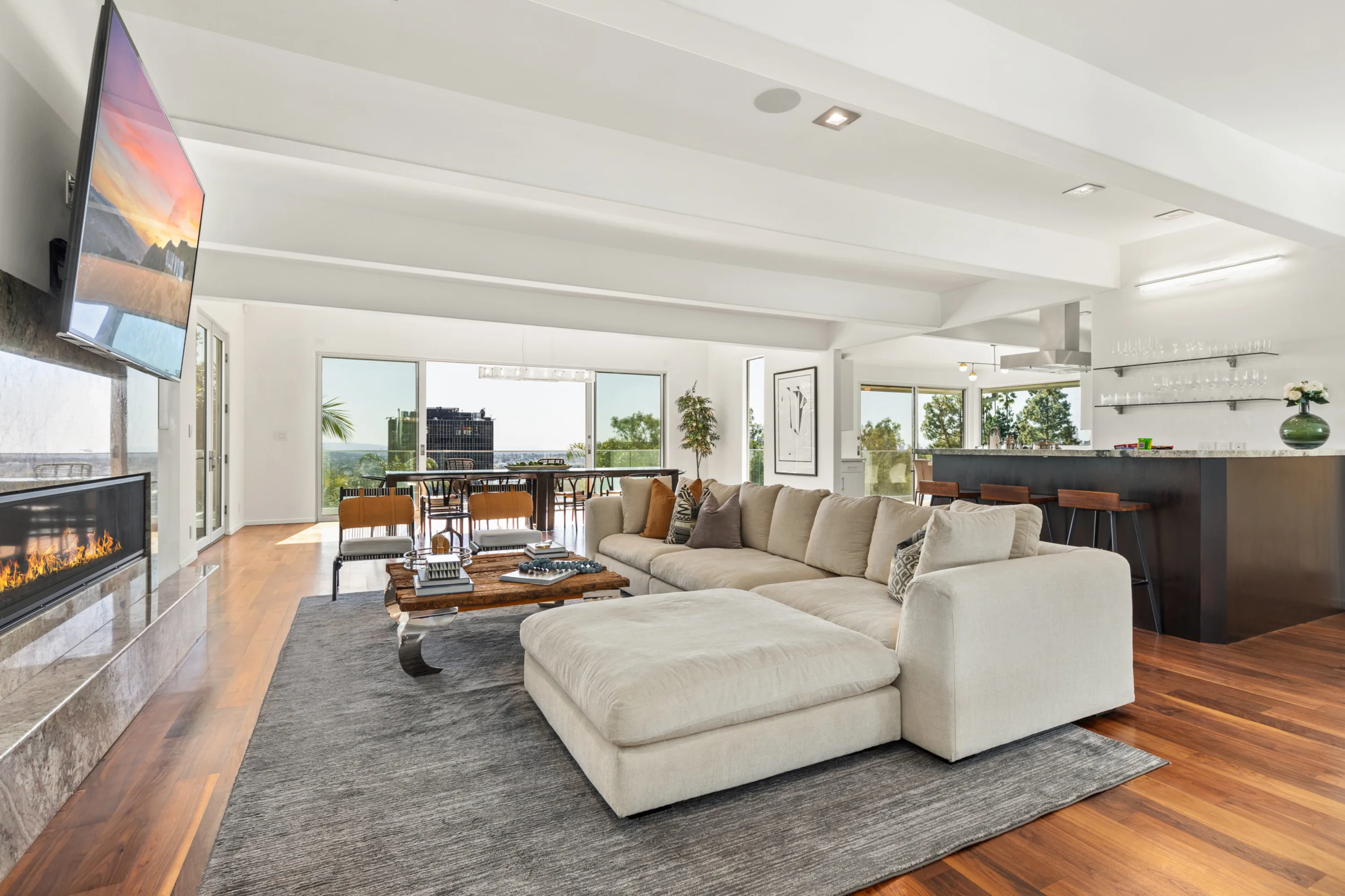 Open-plan great room with sectional sofa, linear fireplace and wall-mounted TV, opening to a city-view terrace