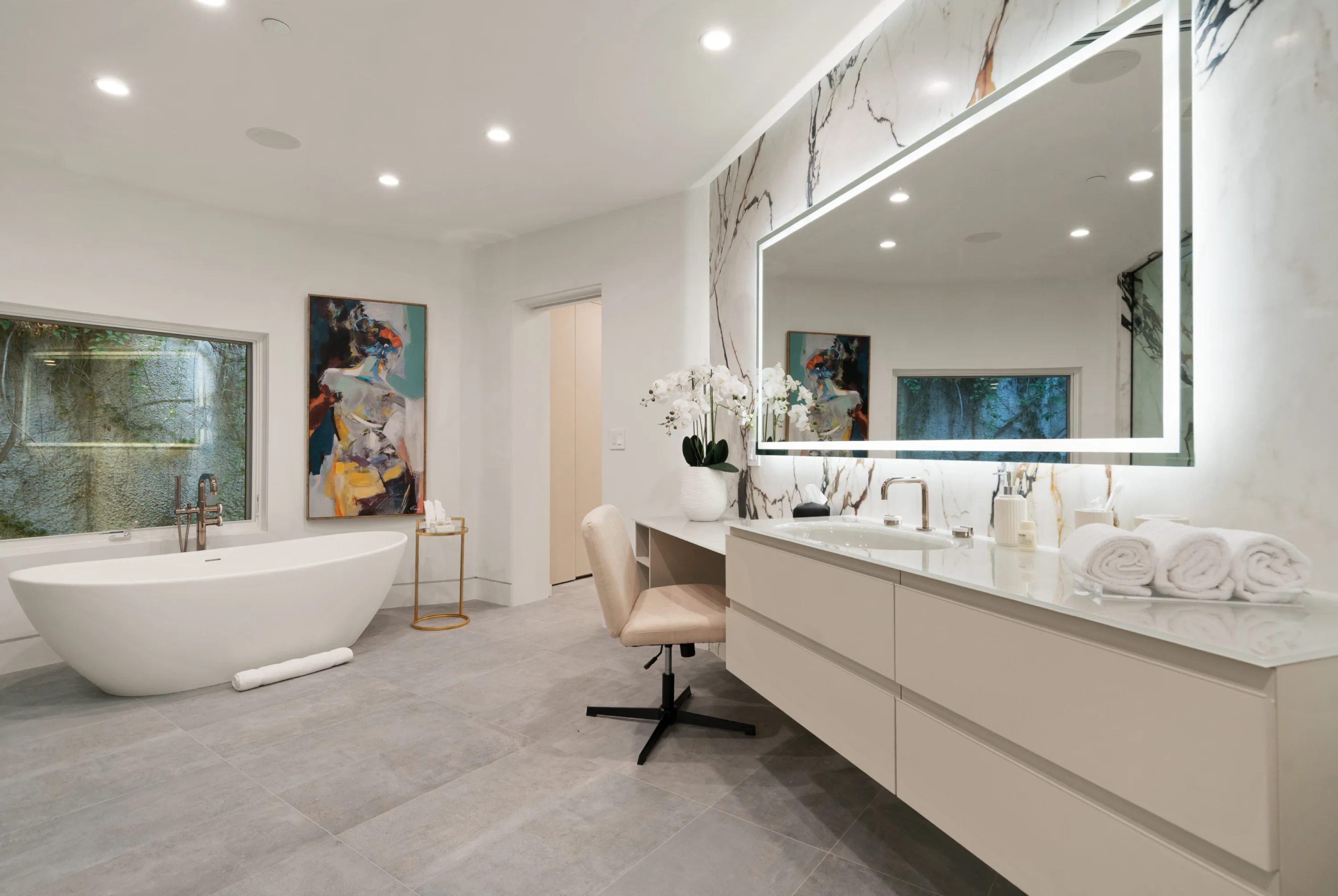 Second primary bath with seated vanity station, rolled towels, orchids and a tub set against abstract artwork