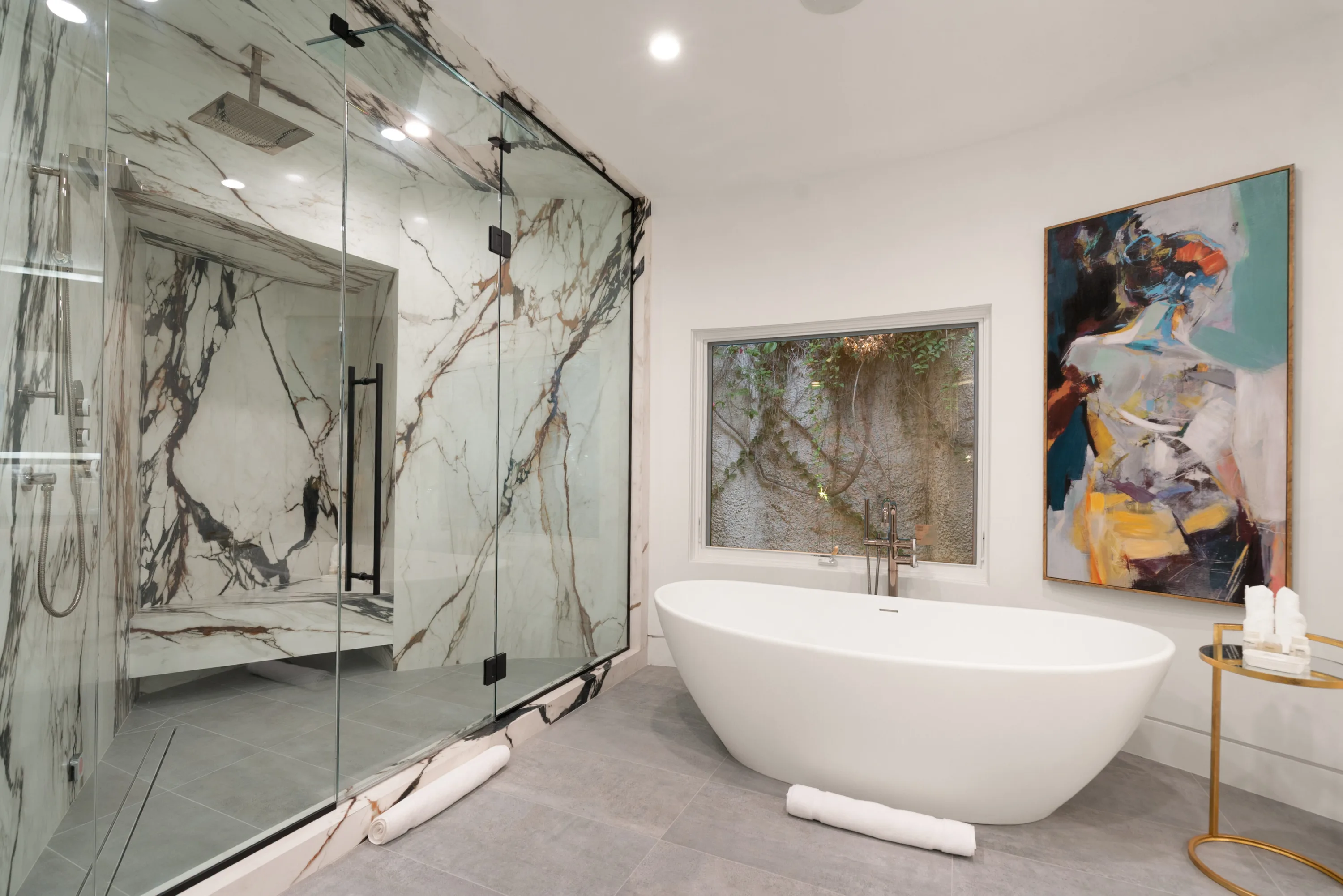 Rain-head marble shower and freestanding tub below a garden window in the ensuite bath