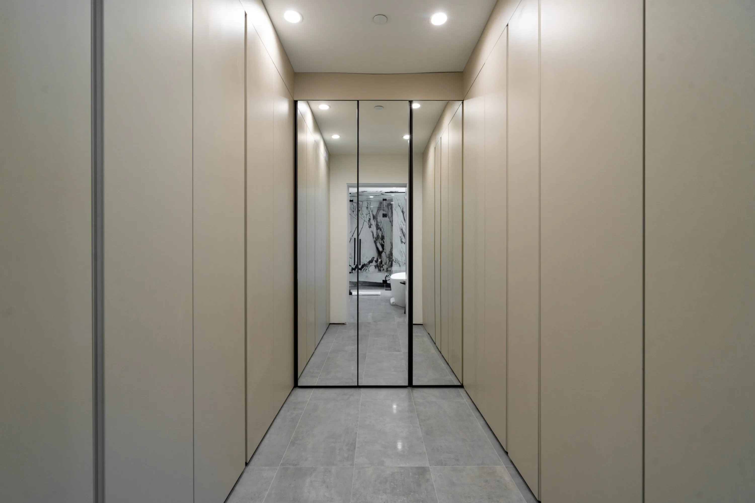 Mirrored dressing corridor of handleless wardrobes leading through to the marble bath