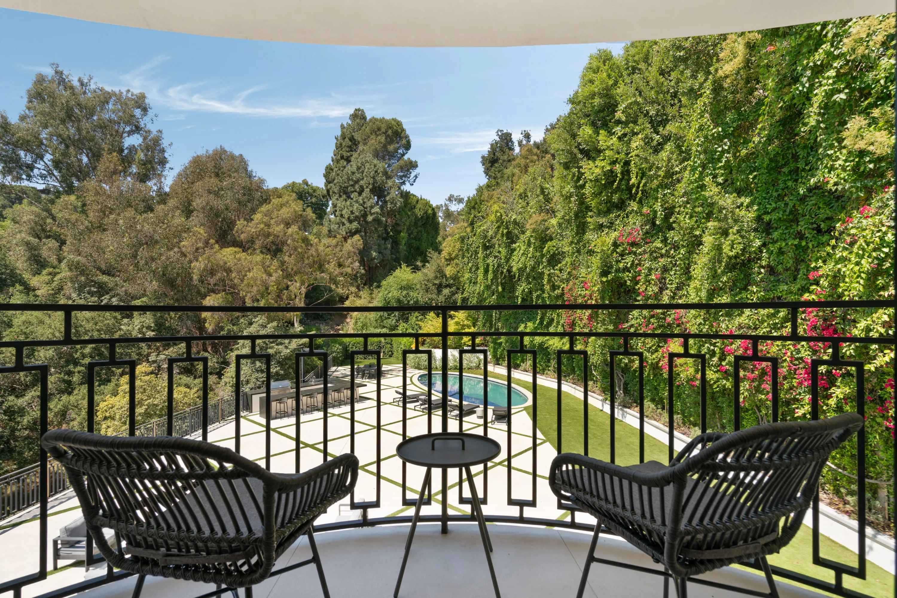 Balcony seating for two overlooking the pool terrace, lawn and bougainvillea-covered hedges below