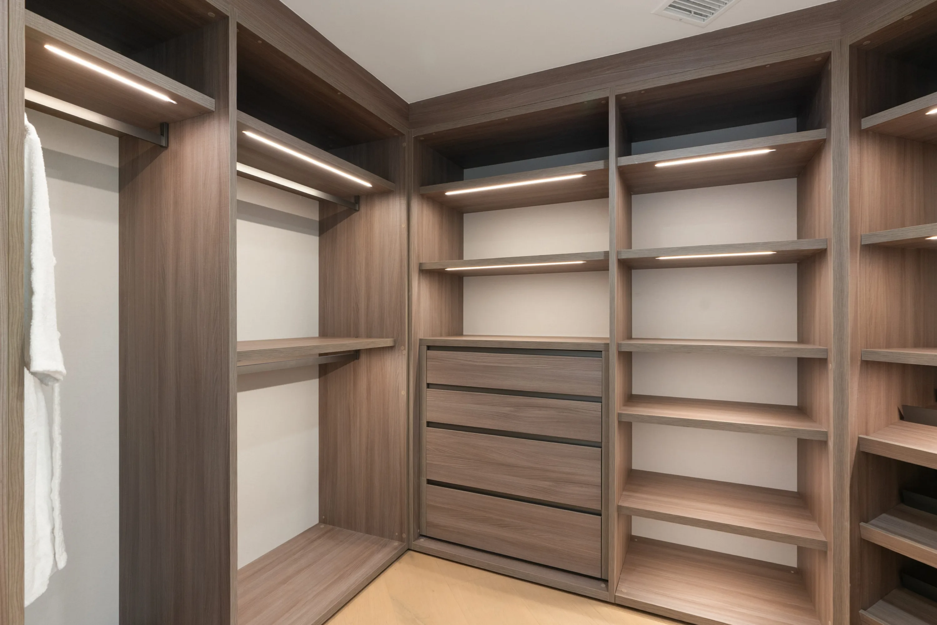 Walk-in wardrobe in warm oak with LED-lit shelving, hanging rails and built-in drawers
