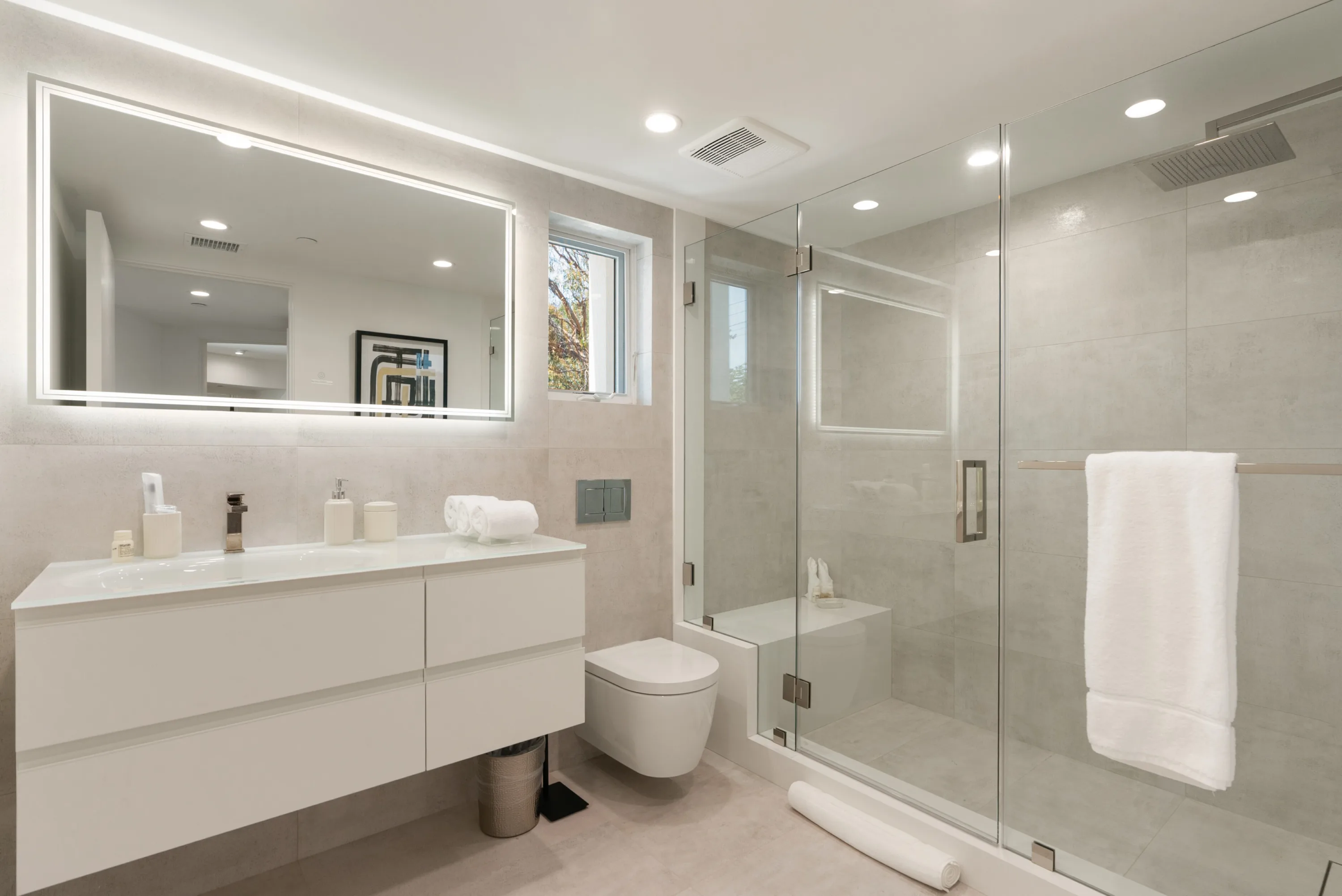 Guest bath with floating white vanity, backlit mirror and glass walk-in shower with bench