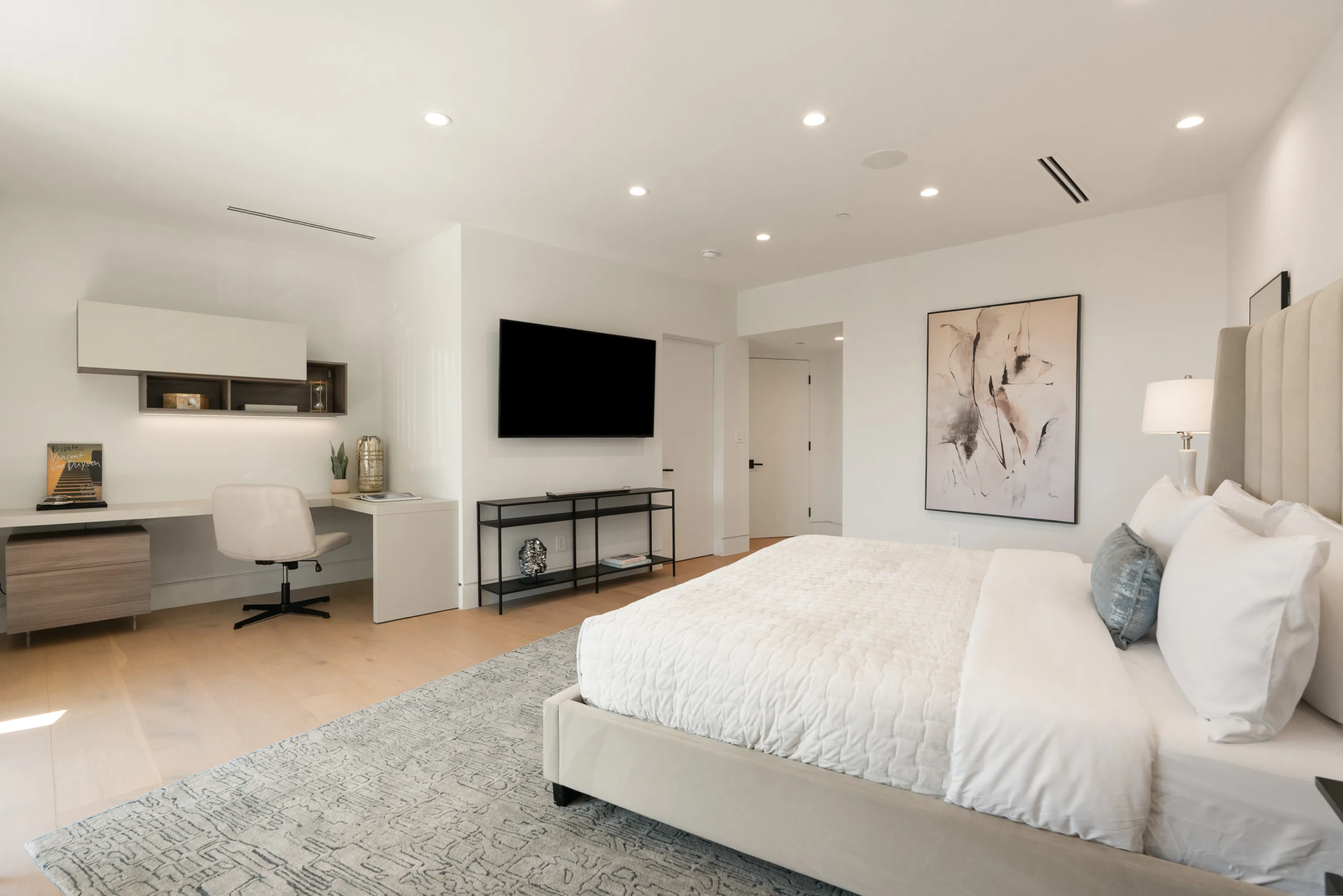 Bedroom suite with built-in desk and wall-mounted TV opposite a king bed dressed in white