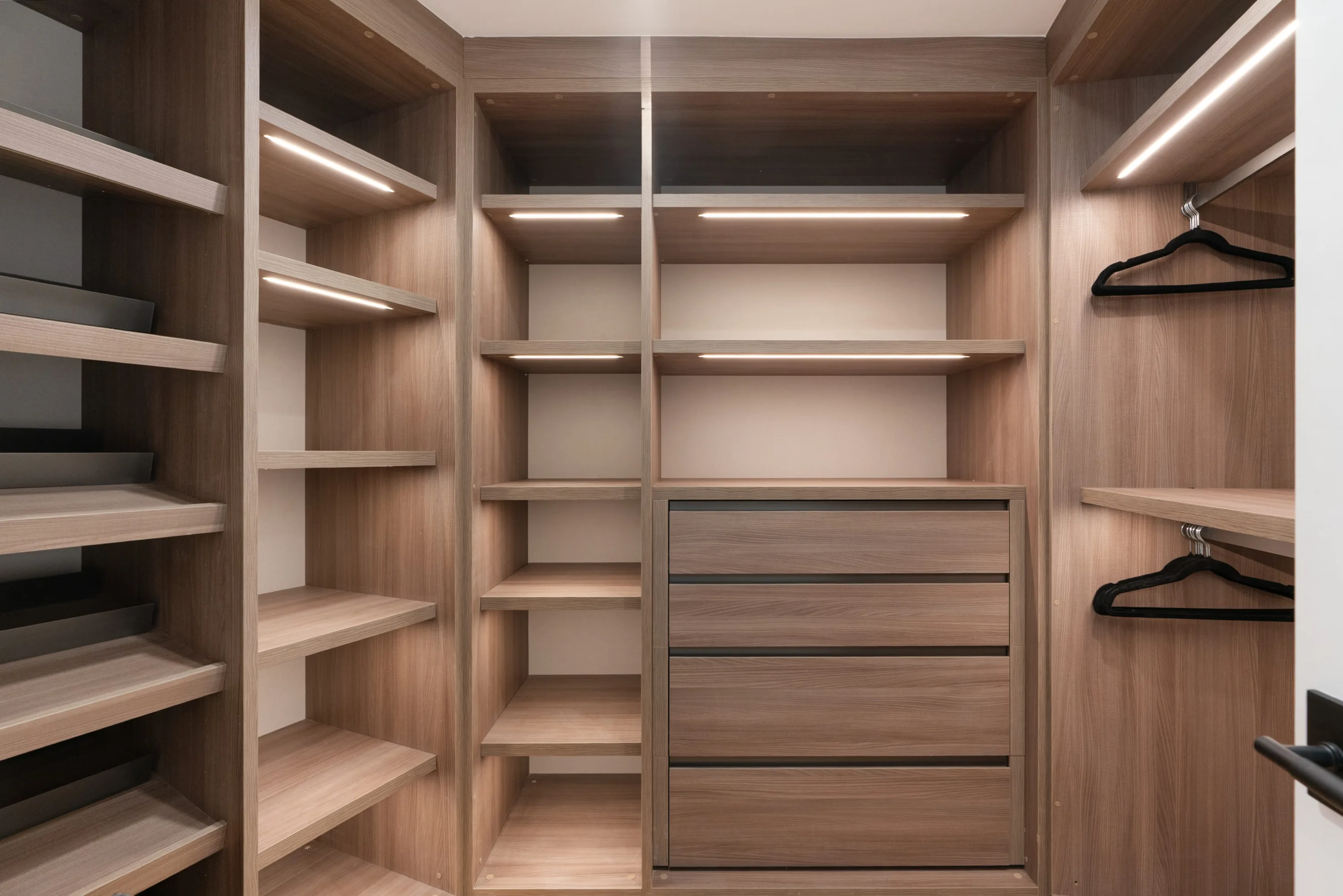 Fitted closet with lit oak shelving, shoe racks and velvet hangers on twin rails