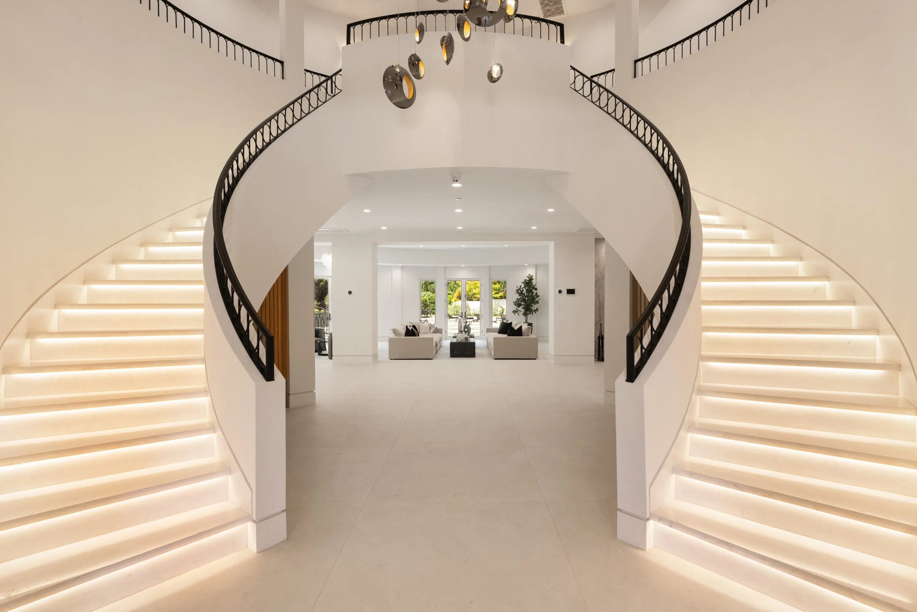 Twin curved staircases with illuminated treads and ironwork rails framing the living room beyond