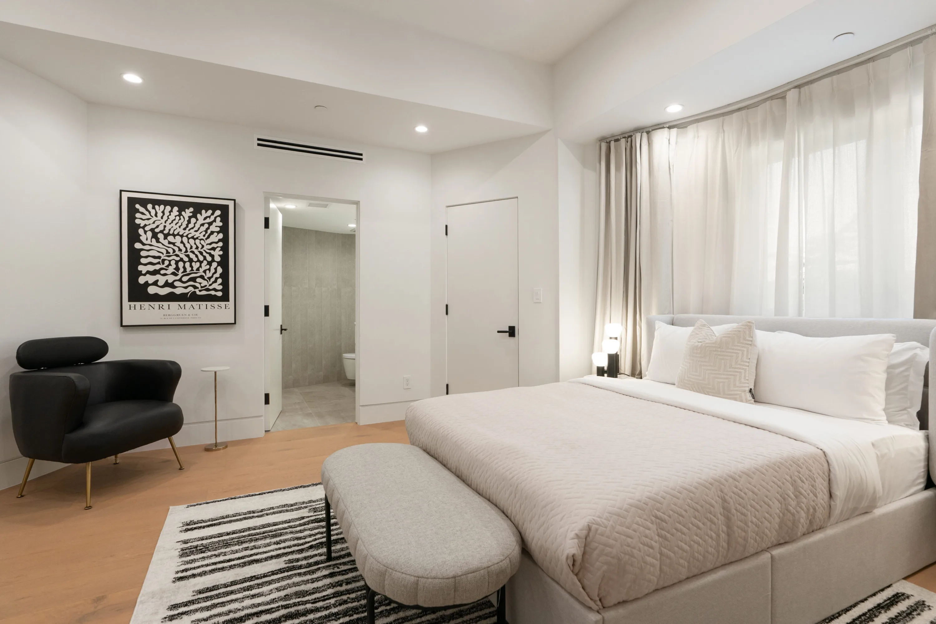 Bedroom with black lounge chair, ensuite doorway and a framed Henri Matisse cut-out print on the wall
