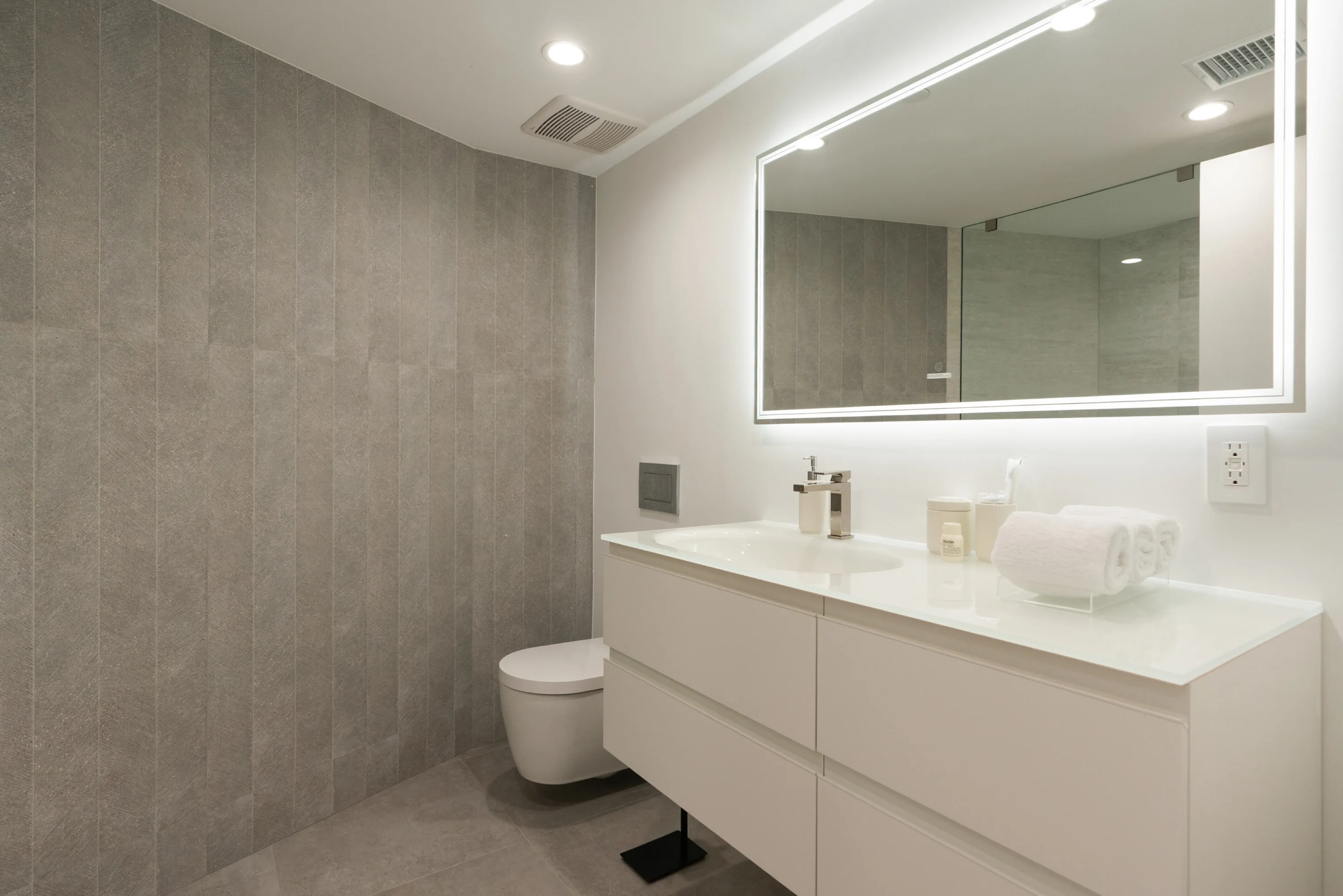 Guest bathroom with floating white vanity, backlit mirror and grey stone-tiled wall