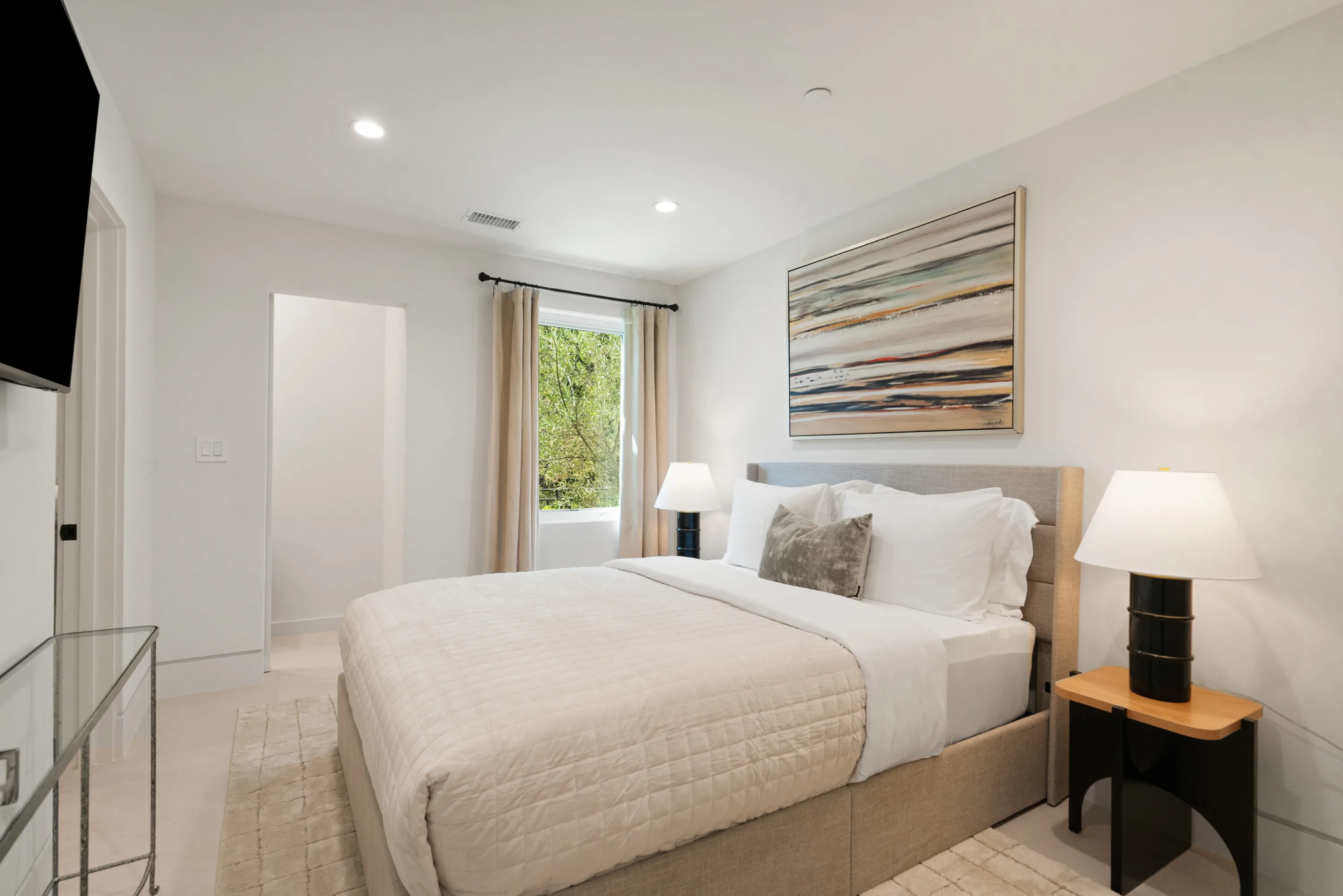 Guest bedroom in cream and grey with abstract canvas above the bed and a leafy window outlook